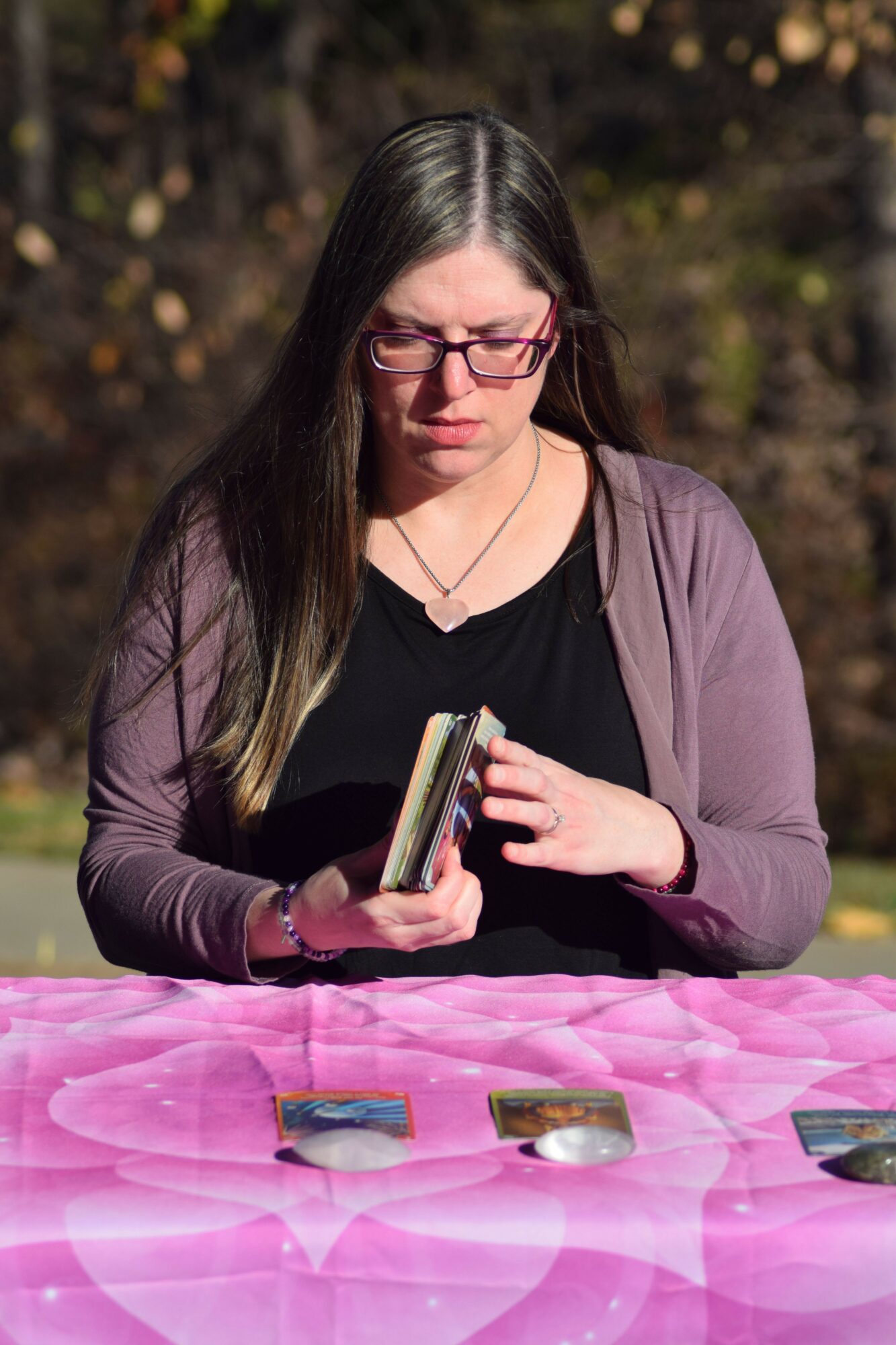 Woman with glasses and long dark hair looking at a phone, sitting at a pink table outdoors.