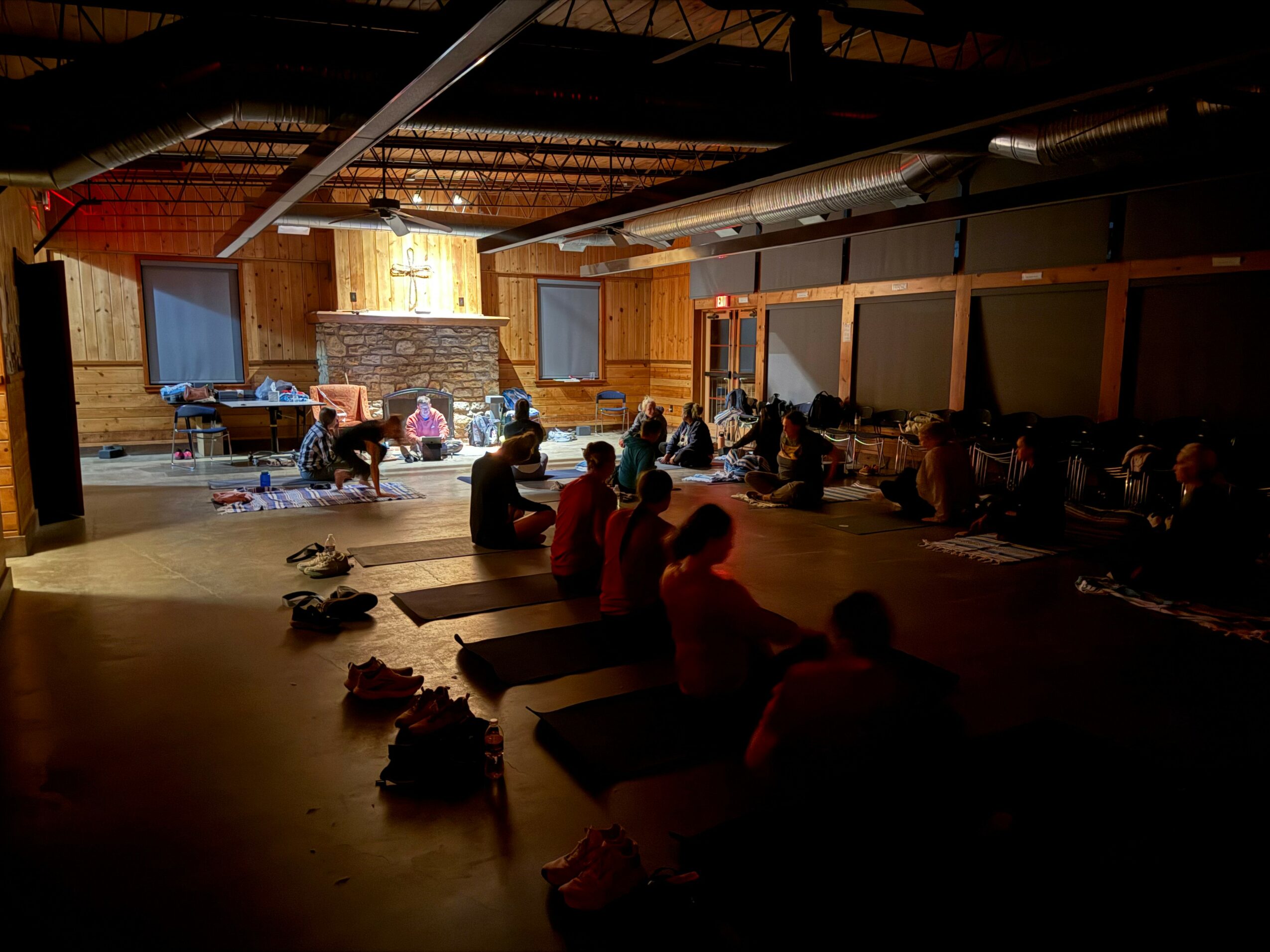 People practicing yoga or meditation in a dimly lit indoor space with wooden walls and a high ceiling.