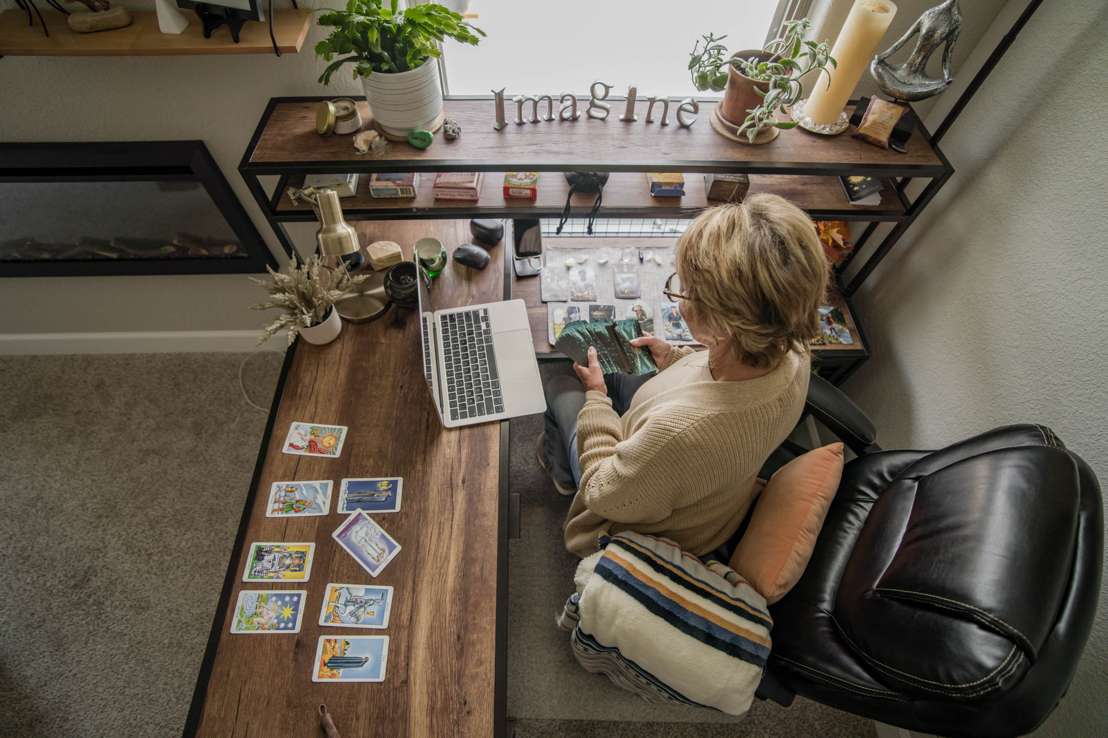 Person with short hair and glasses sits at a desk, playing a card game with cards spread out.