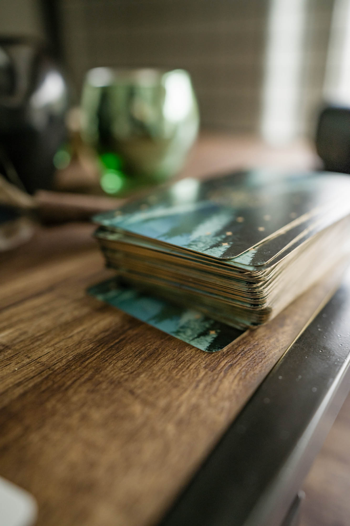 Stack of photographs on a wooden table with blurred background including a green glass and a window.