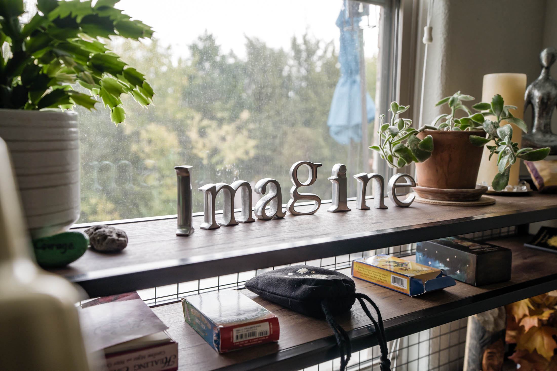 Decorative letters spelling 'Imagine' on a windowsill with plants and outdoor view.
