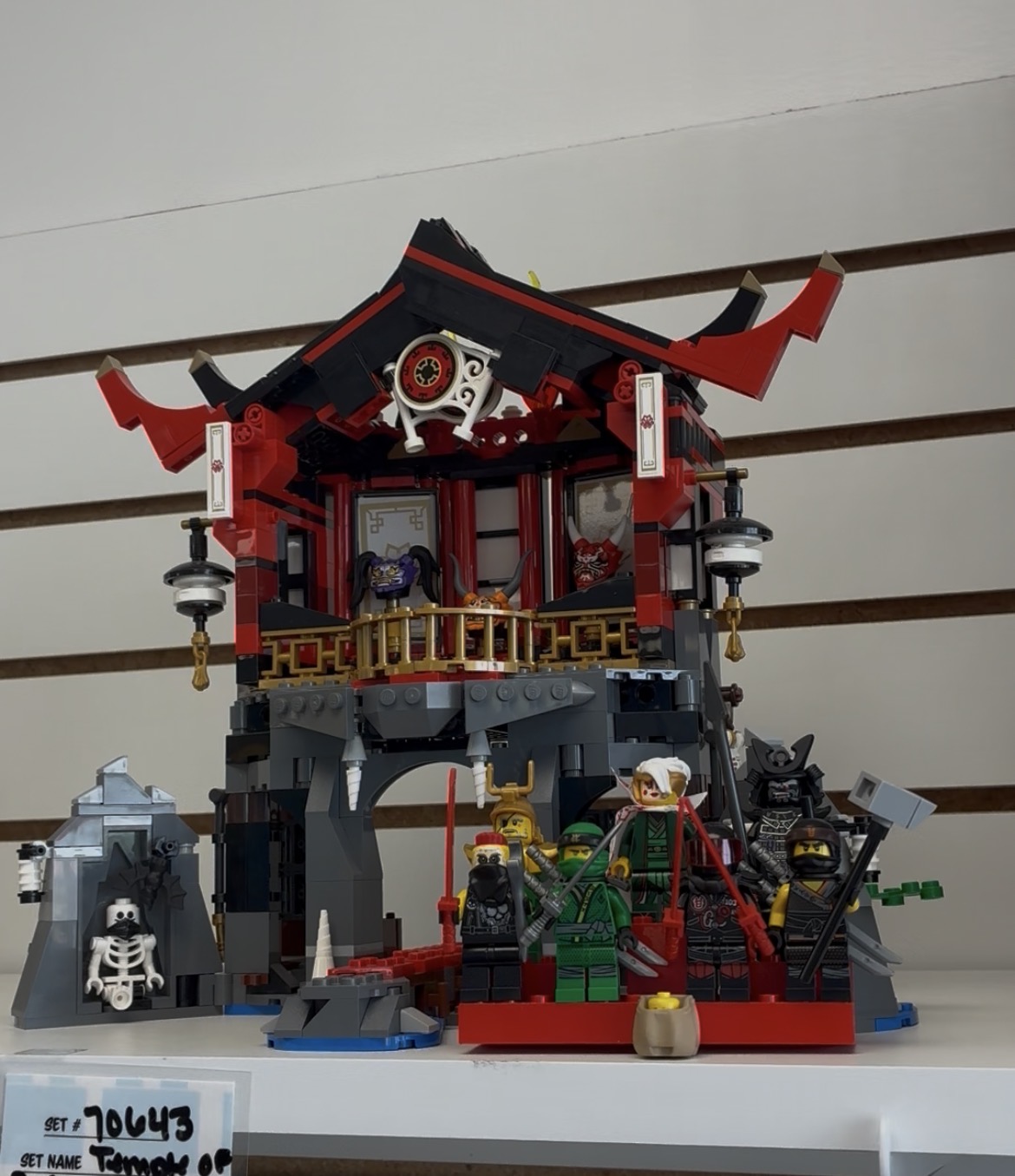 Lego set depicting a traditional Asian building with characters and accessories in front, on a white surface.