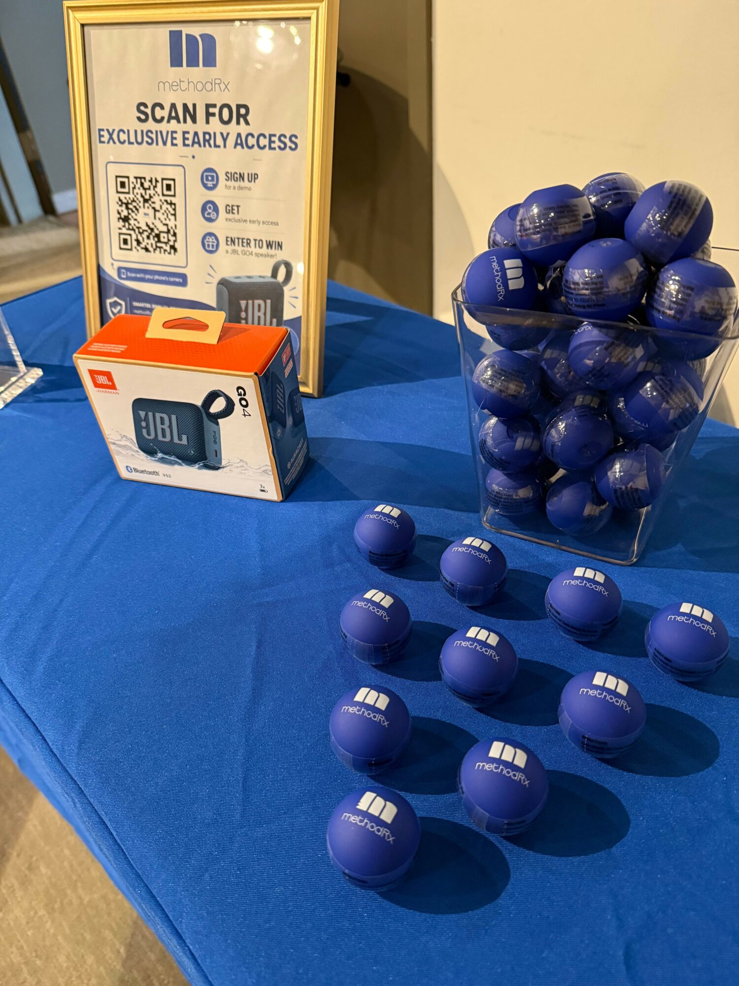 Blue JBL earbuds box, blue balls in a glass container, and scattered blue balls on a blue tablecloth.