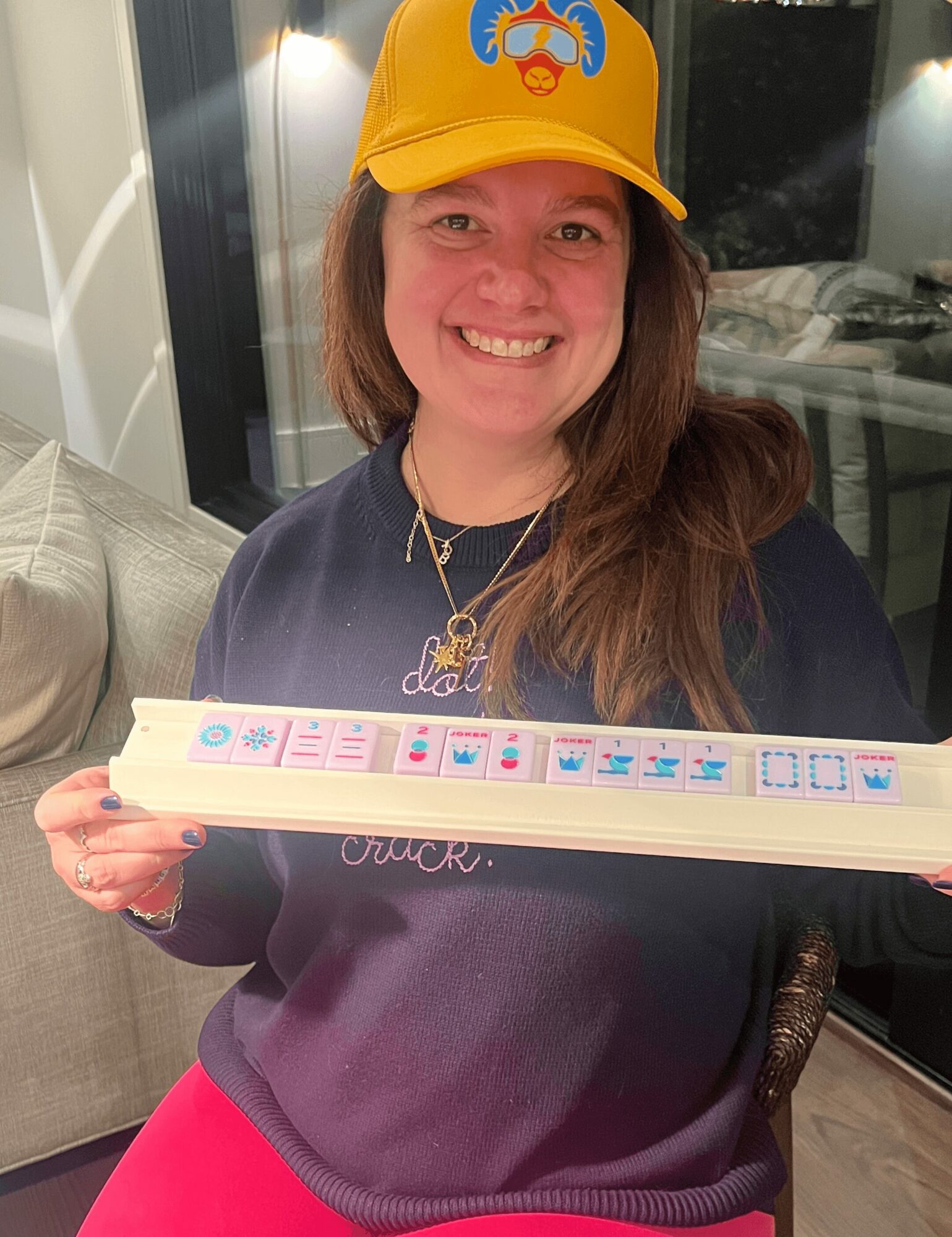 Woman wearing a yellow cap and dark sweatshirt, smiling, holding a long white object with colorful designs.