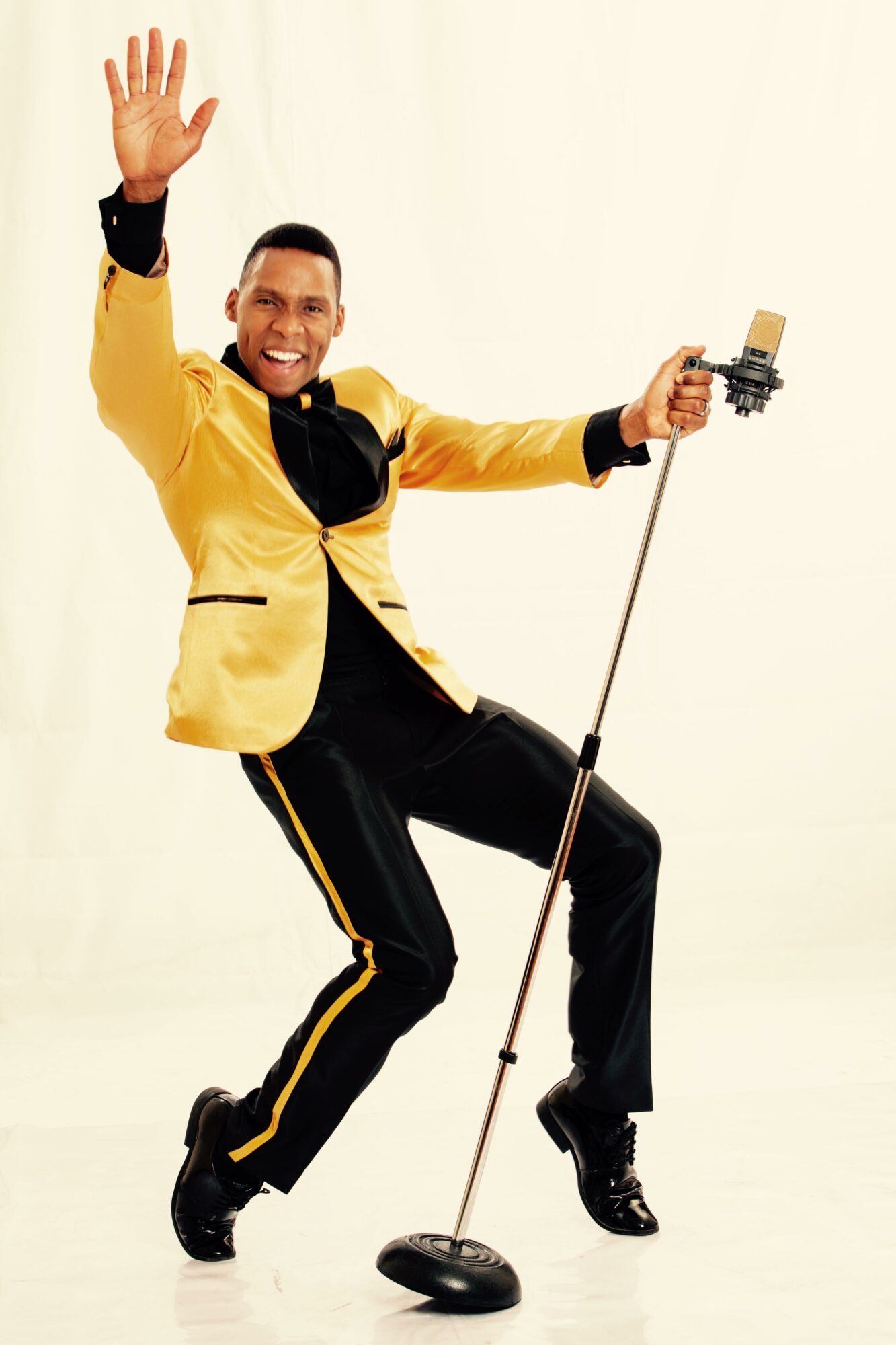 Person in yellow jacket dancing with a microphone stand, smiling, against a plain background.