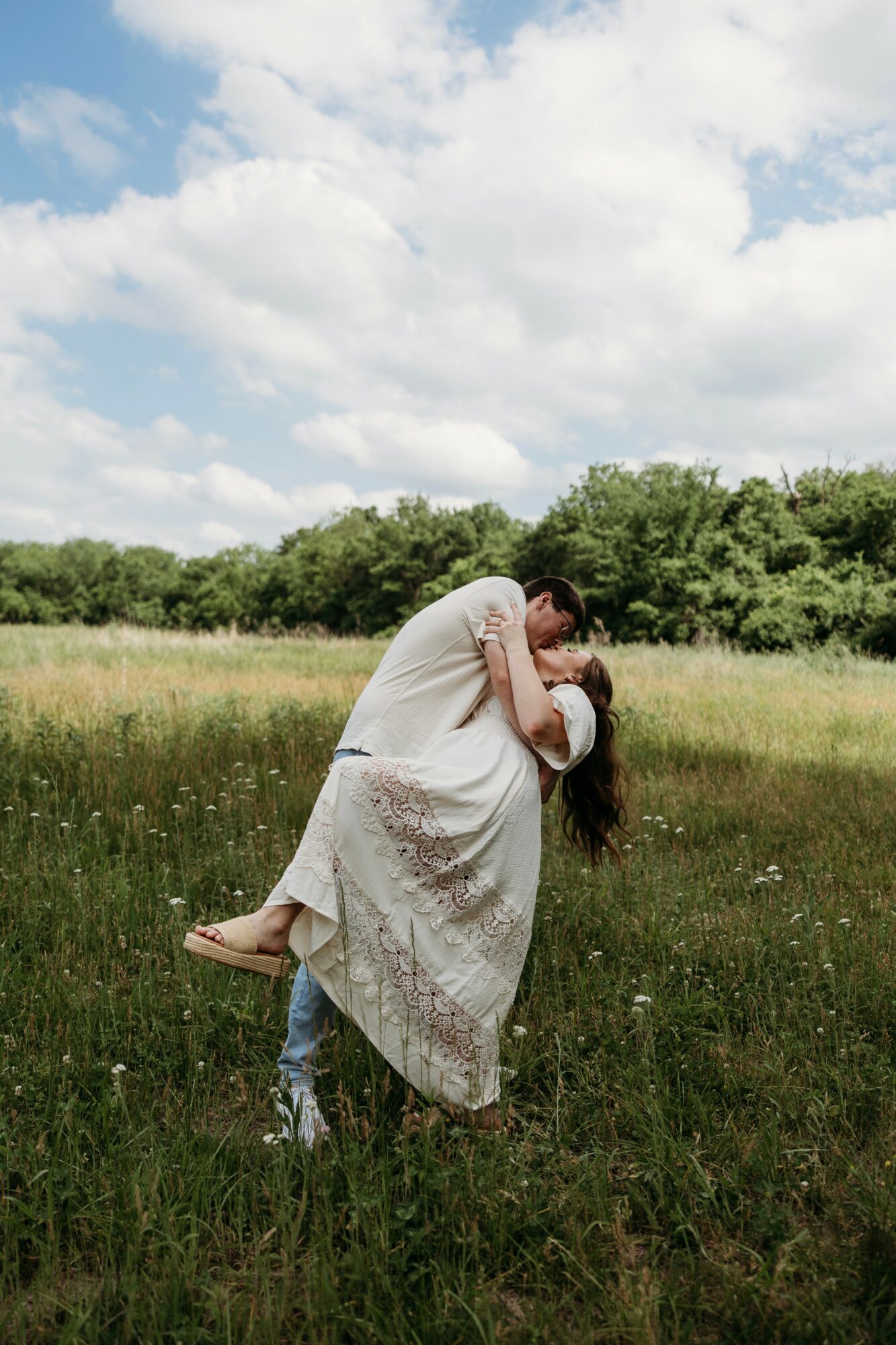 A person lifts another person in a field with green grass and trees, under a partly cloudy sky.