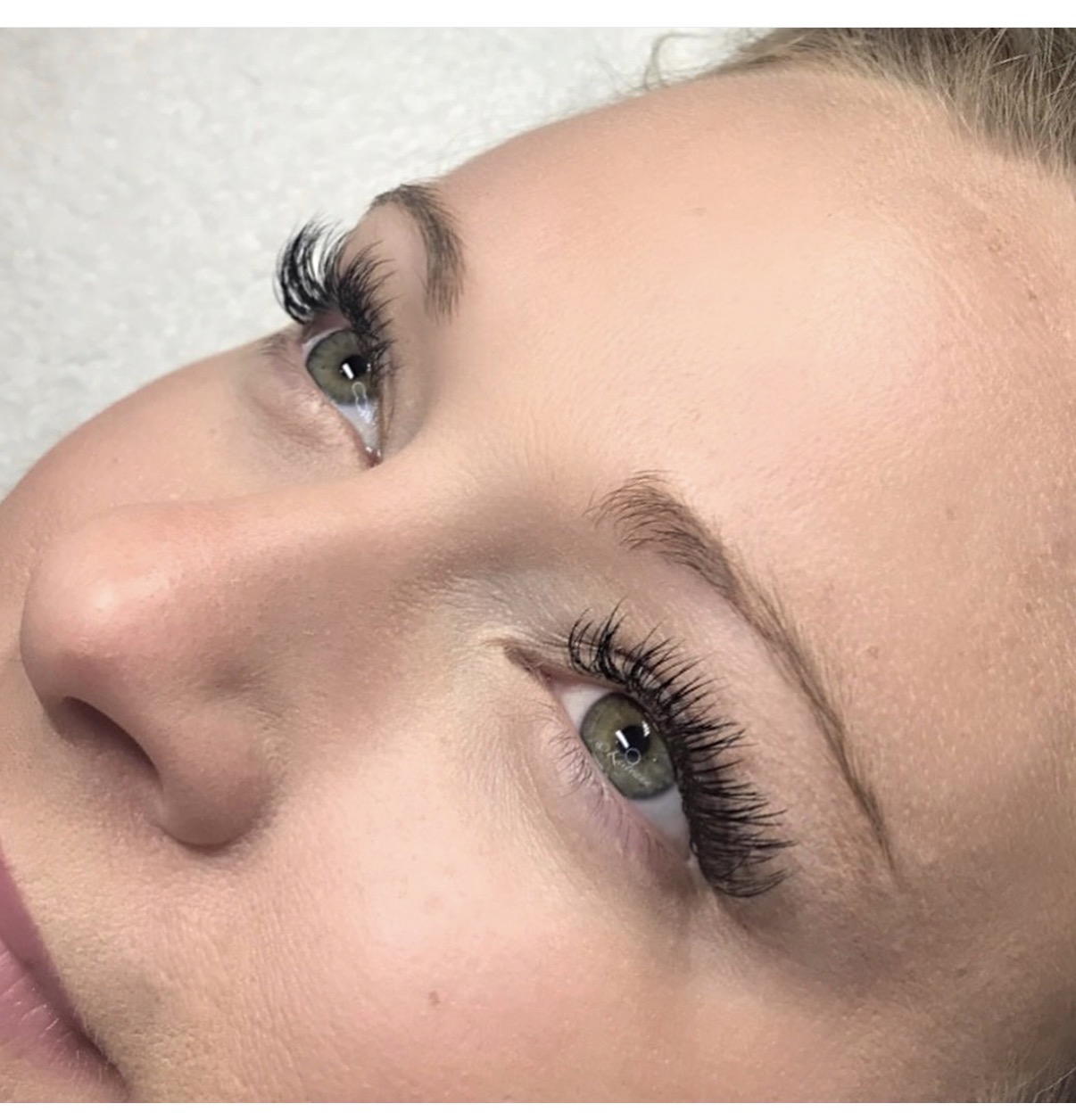 Close-up of a woman's face showing her eyes, eyebrows, and part of her nose, with makeup and long eyelashes.
