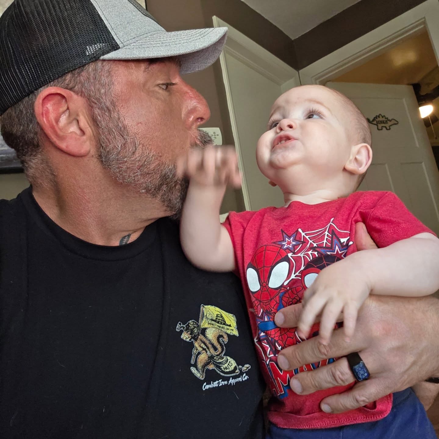 Adult holding a baby, both making playful faces, indoors with a door in the background.