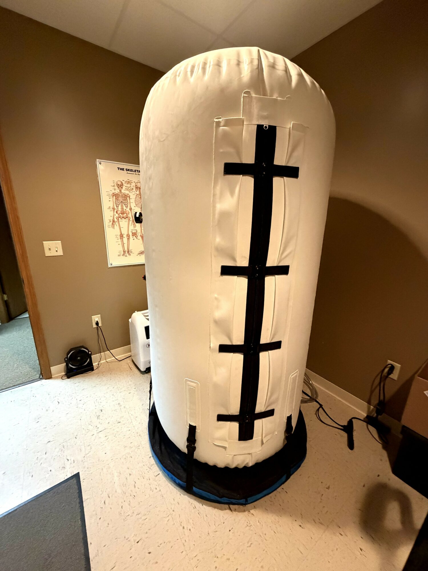Inflatable medical dummy with a vertical black line and horizontal markings, standing in a room with brown walls.