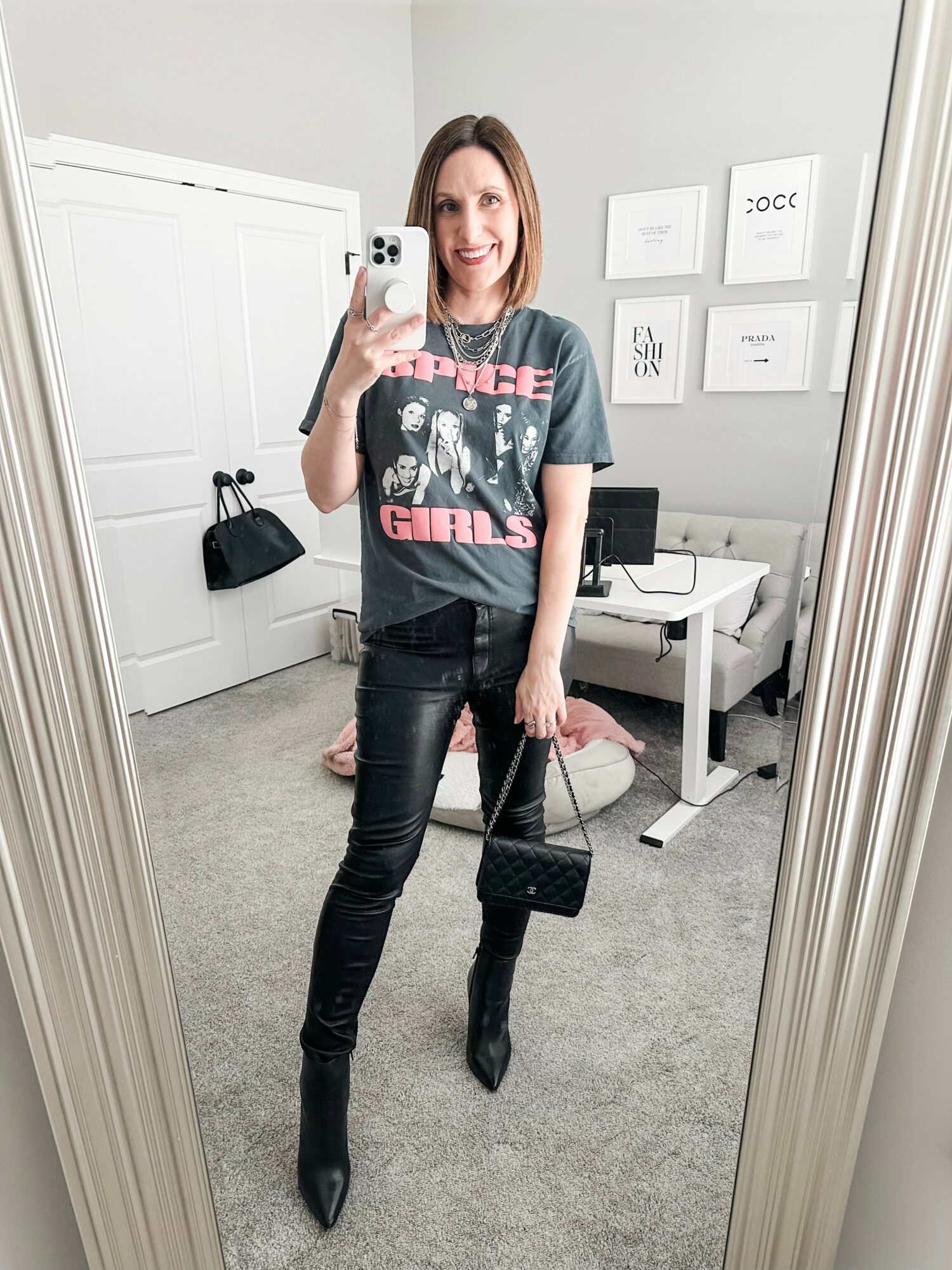 Woman taking a mirror selfie in a room with a desk, computer, and framed pictures on the wall.
