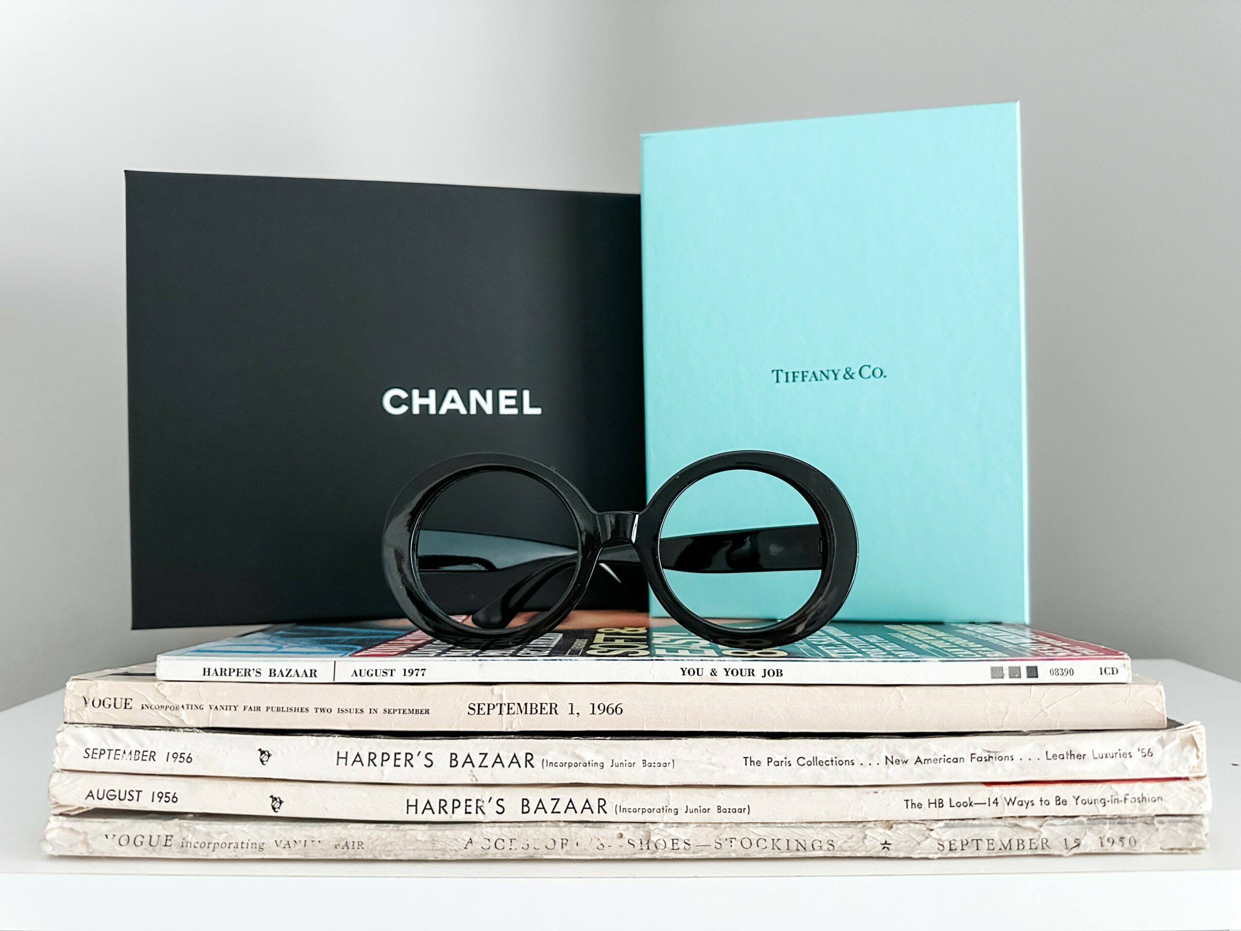 Stack of magazines with black and blue booklets and round glasses on top, against a plain background.