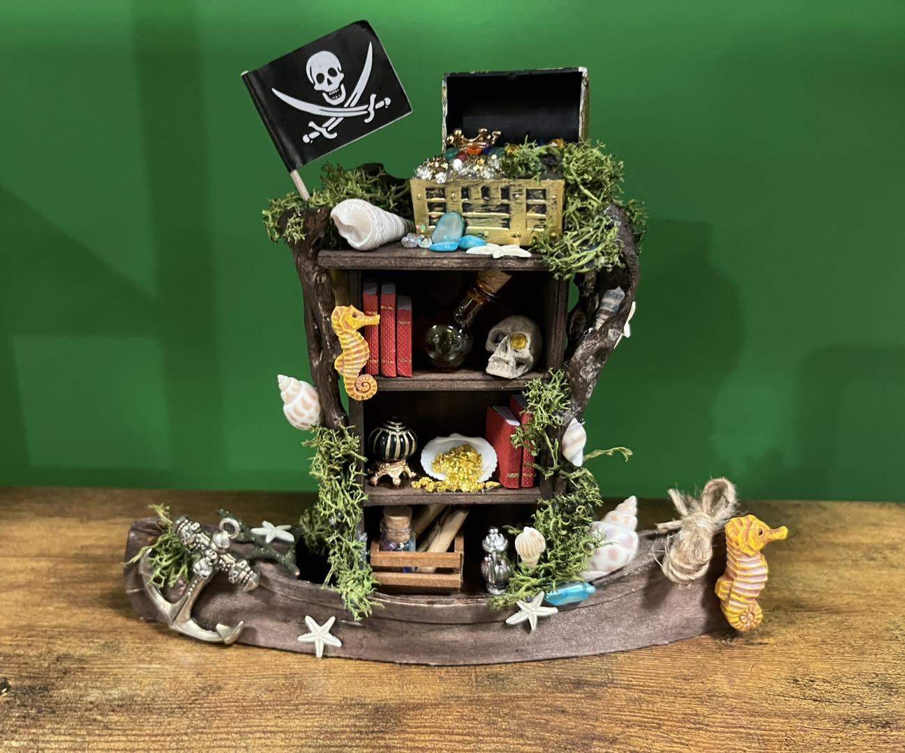 Decorative pirate-themed display with a small wooden ship, treasure chest, skull flag, and sea creatures on a wooden surface.