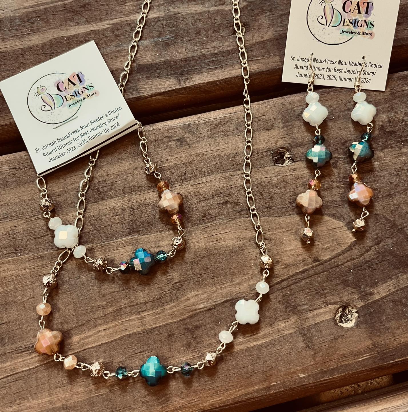 Necklace and earrings with beads and charms on a wooden surface, jewelry tags attached.