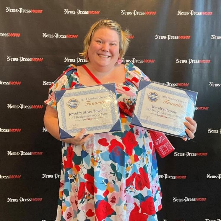 Smiling woman holding two award certificates in front of a black backdrop with 'News-Press' logo, wearing a colorful floral dress.