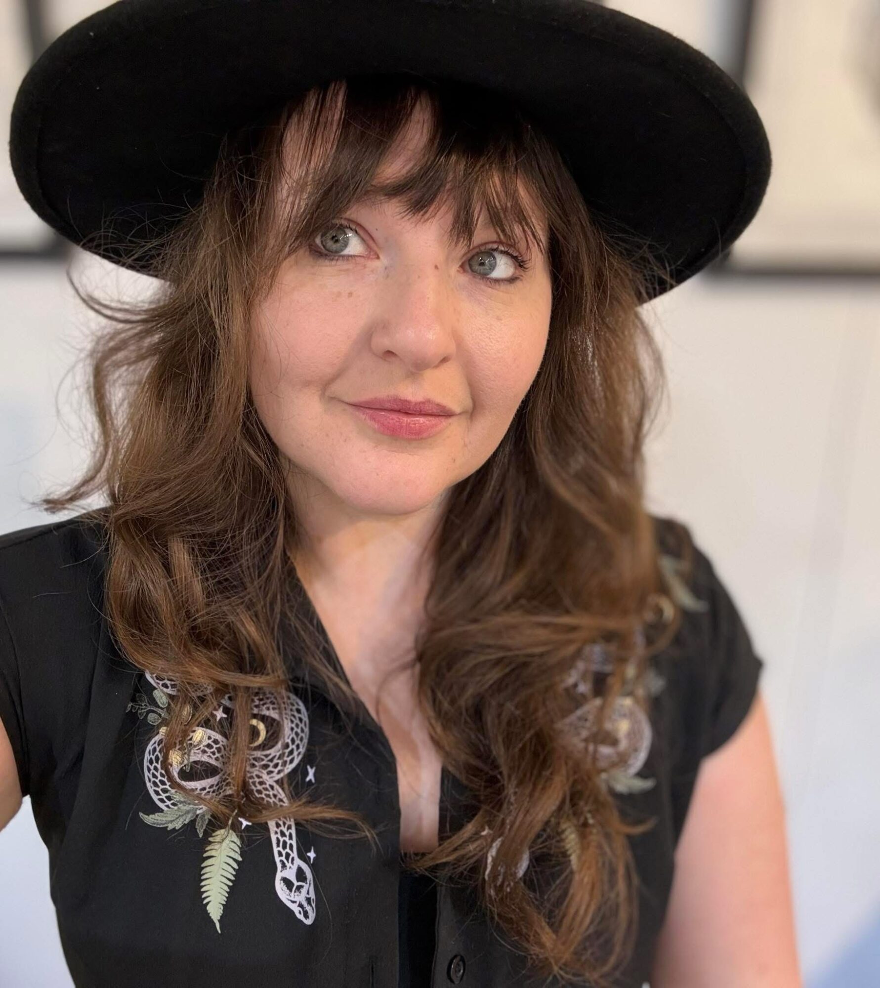 Woman with wavy hair wearing a wide-brimmed hat and embroidered black top, looking to the side.