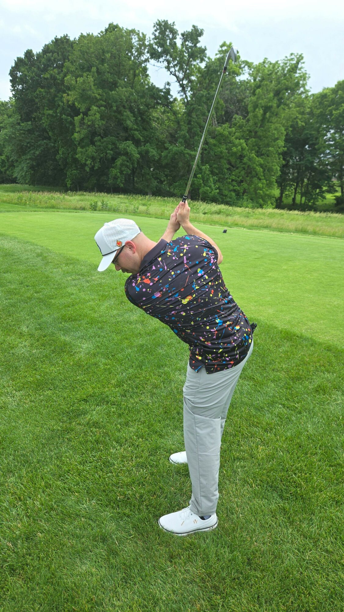 Person preparing to swing a golf club on a grassy field with trees in the background.
