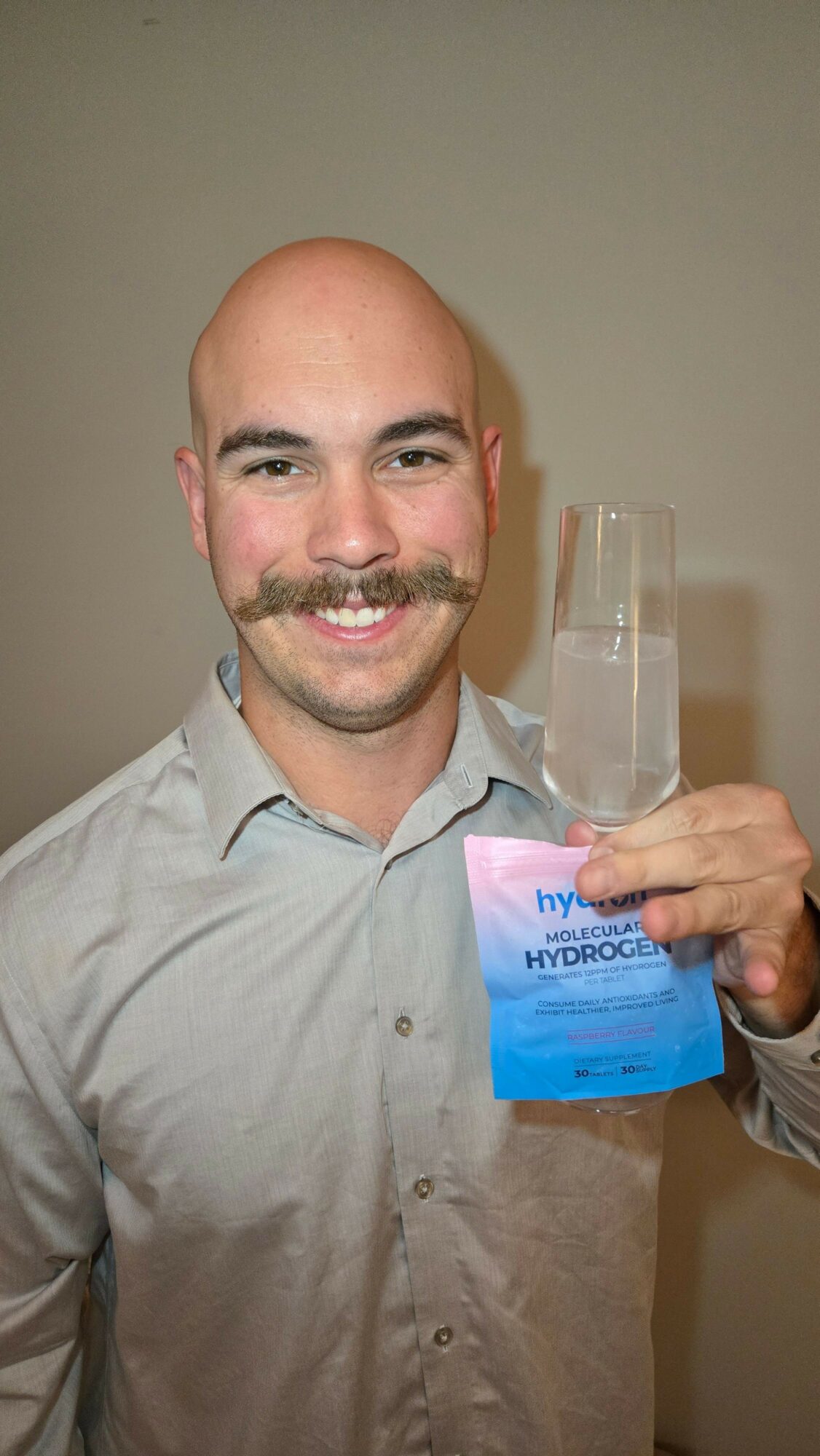 Man with a bald head and beard holding a plastic water bottle, smiling, wearing a light gray shirt.