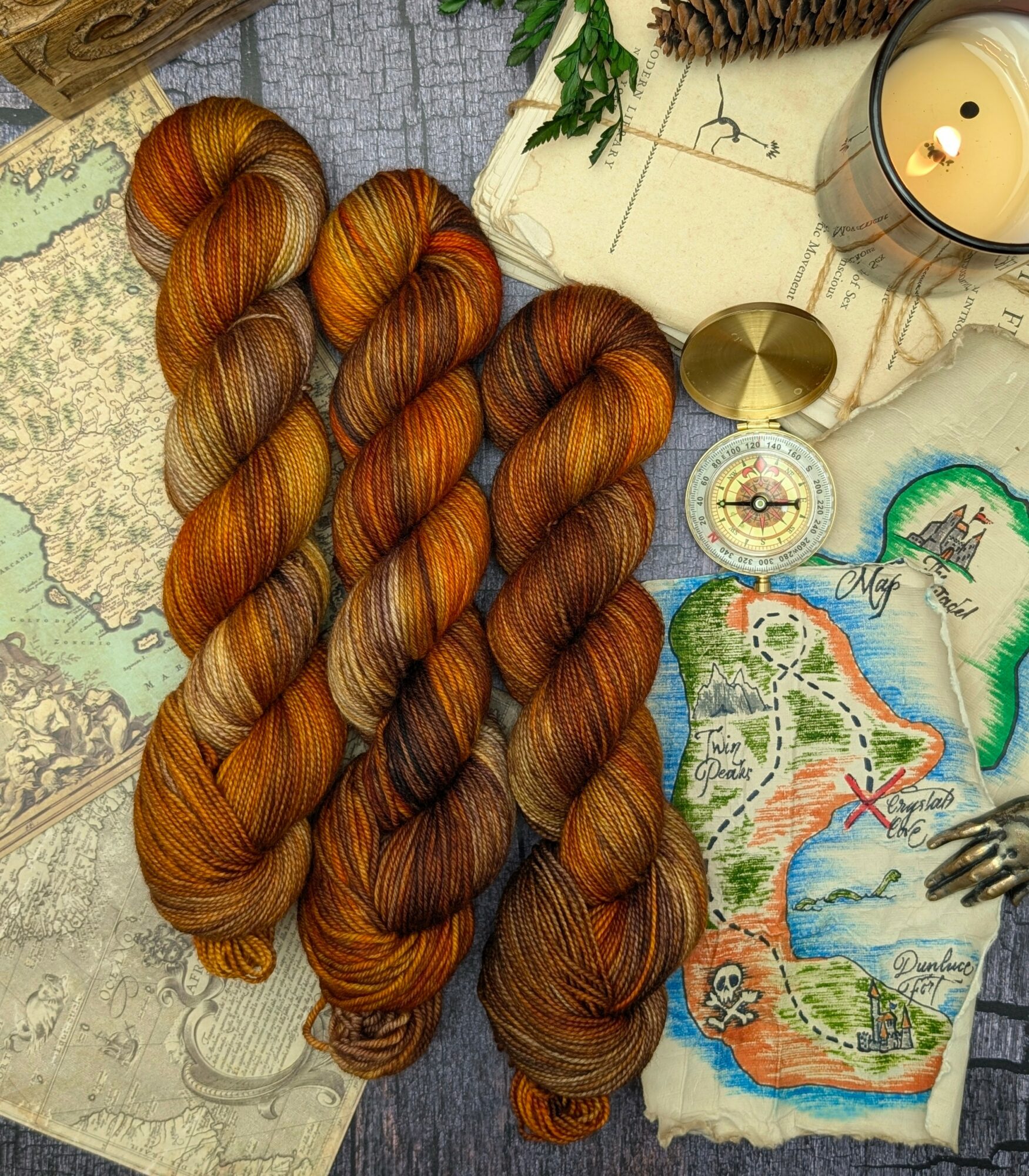 Four skeins of multicolored yarn in shades of orange, brown, and gold, arranged on a map with candles and decorative items.
