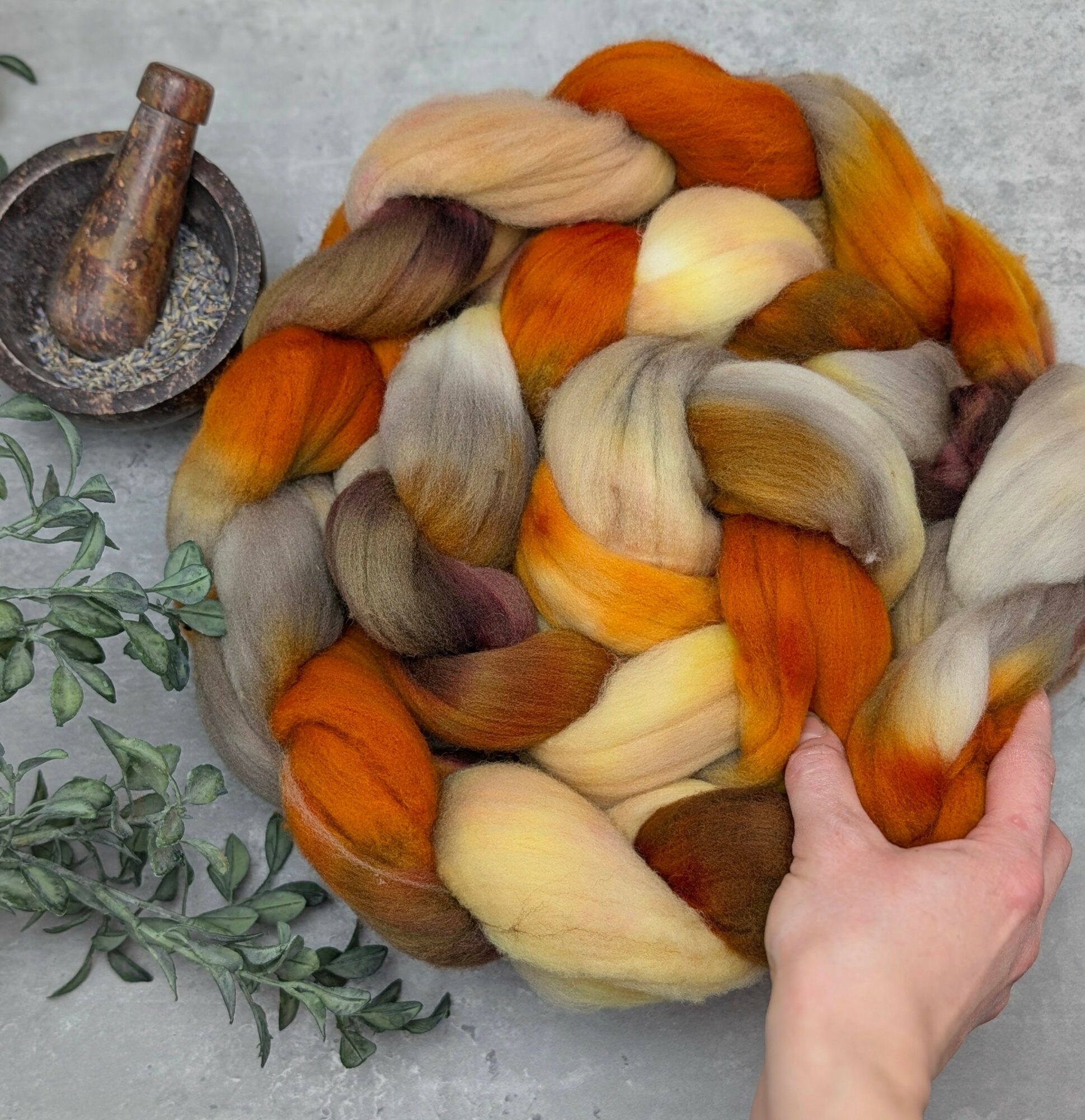 Colorful wool roving in shades of orange, cream, gray, and brown, arranged in a circular shape with a hand holding it.