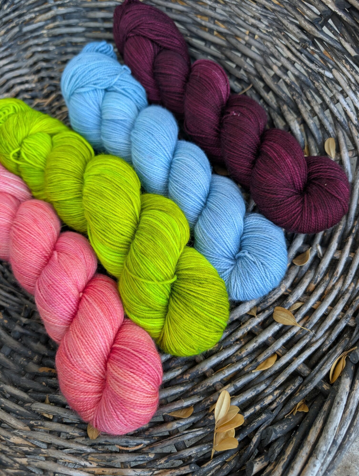 Colorful skeins of yarn in pink, green, blue, and purple on a woven basket surface.