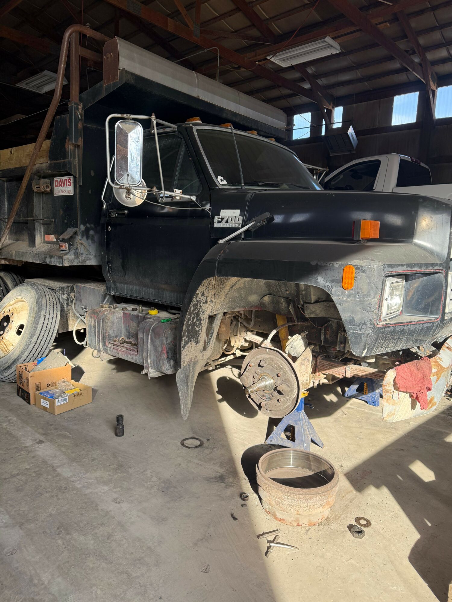 Black truck parked in a workshop with tools and equipment around it, sunlight casting shadows.
