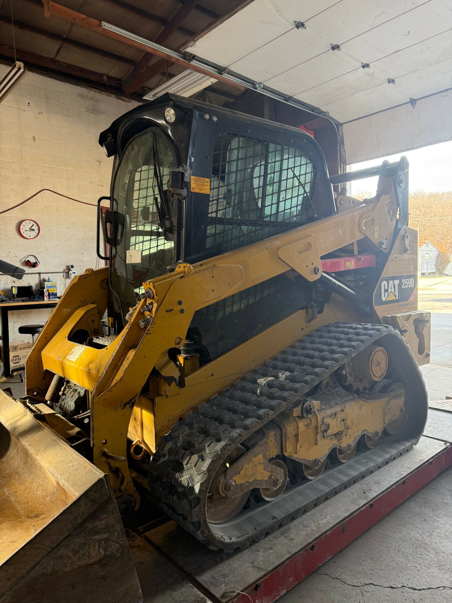 Small yellow tracked construction vehicle inside a garage, viewed from the side, with a black protective cage around the operator's area.