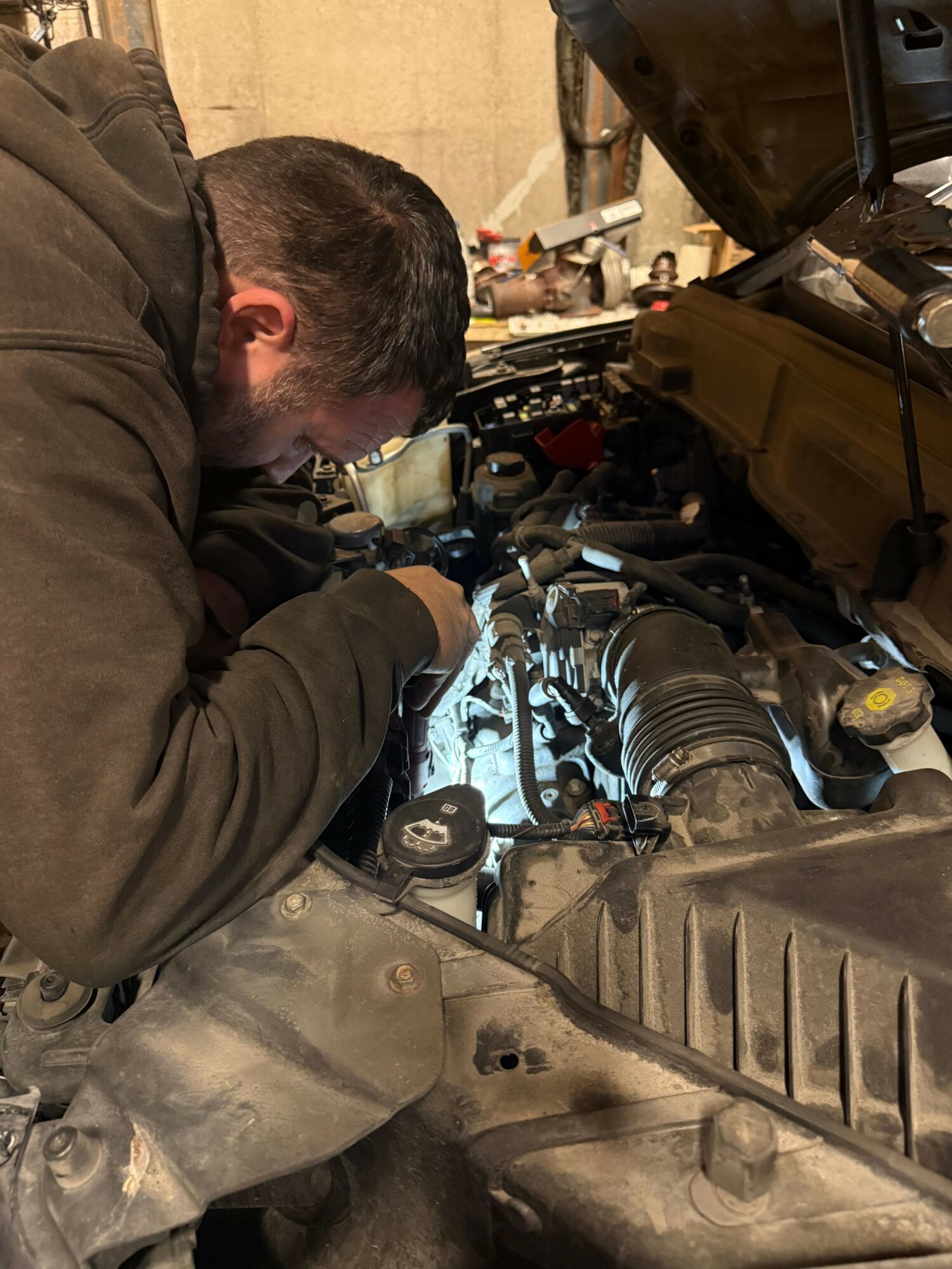 Person working on a vehicle engine, focusing on engine components, in a garage or workshop setting.