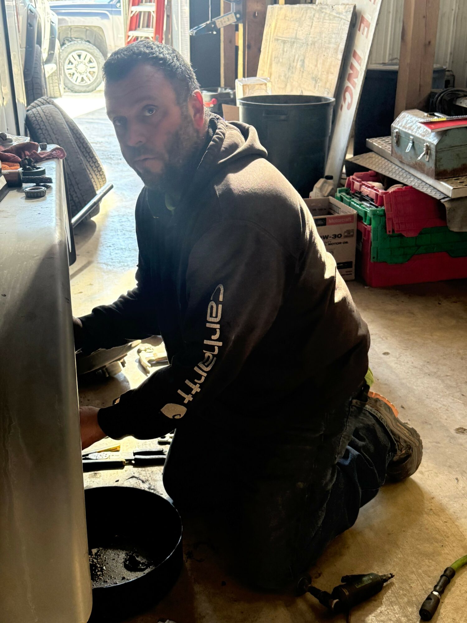 Person kneeling on the ground in a store, surrounded by tires and shelves, looking at the camera.