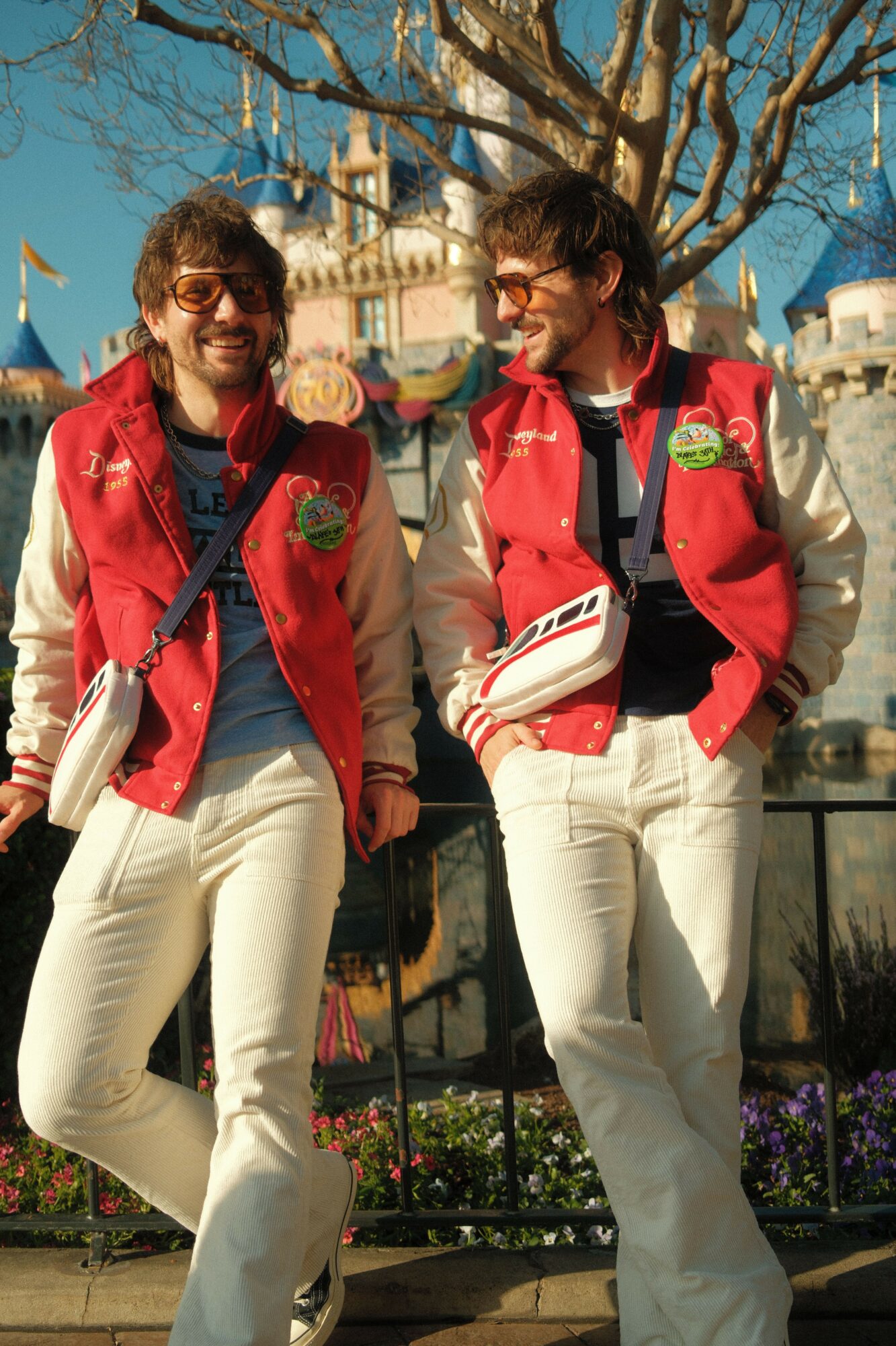 Two women in red jackets and white pants standing outdoors, smiling and talking, with trees and buildings in background.
