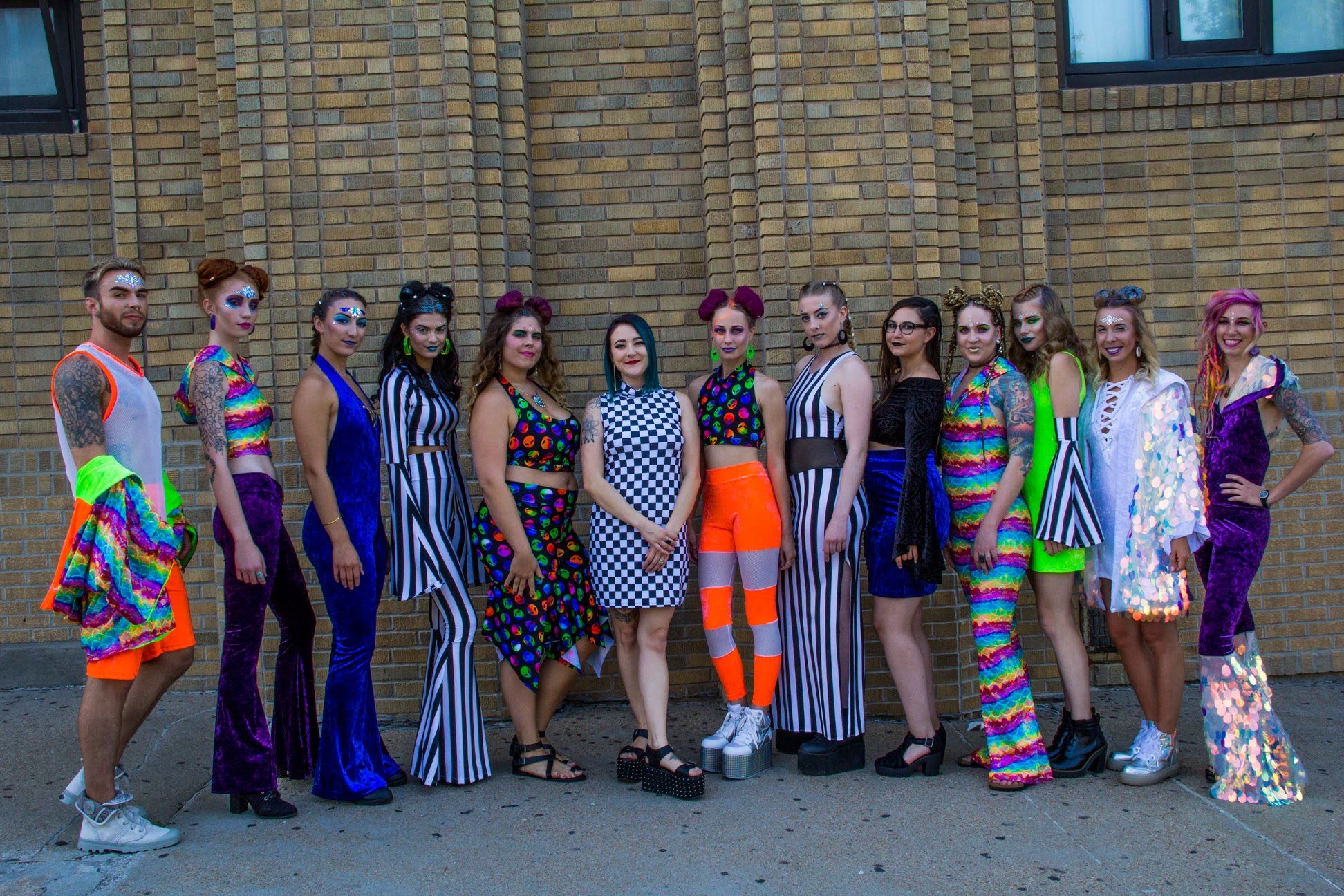 Group of people in colorful, striped, and patterned outfits standing against a brick wall.