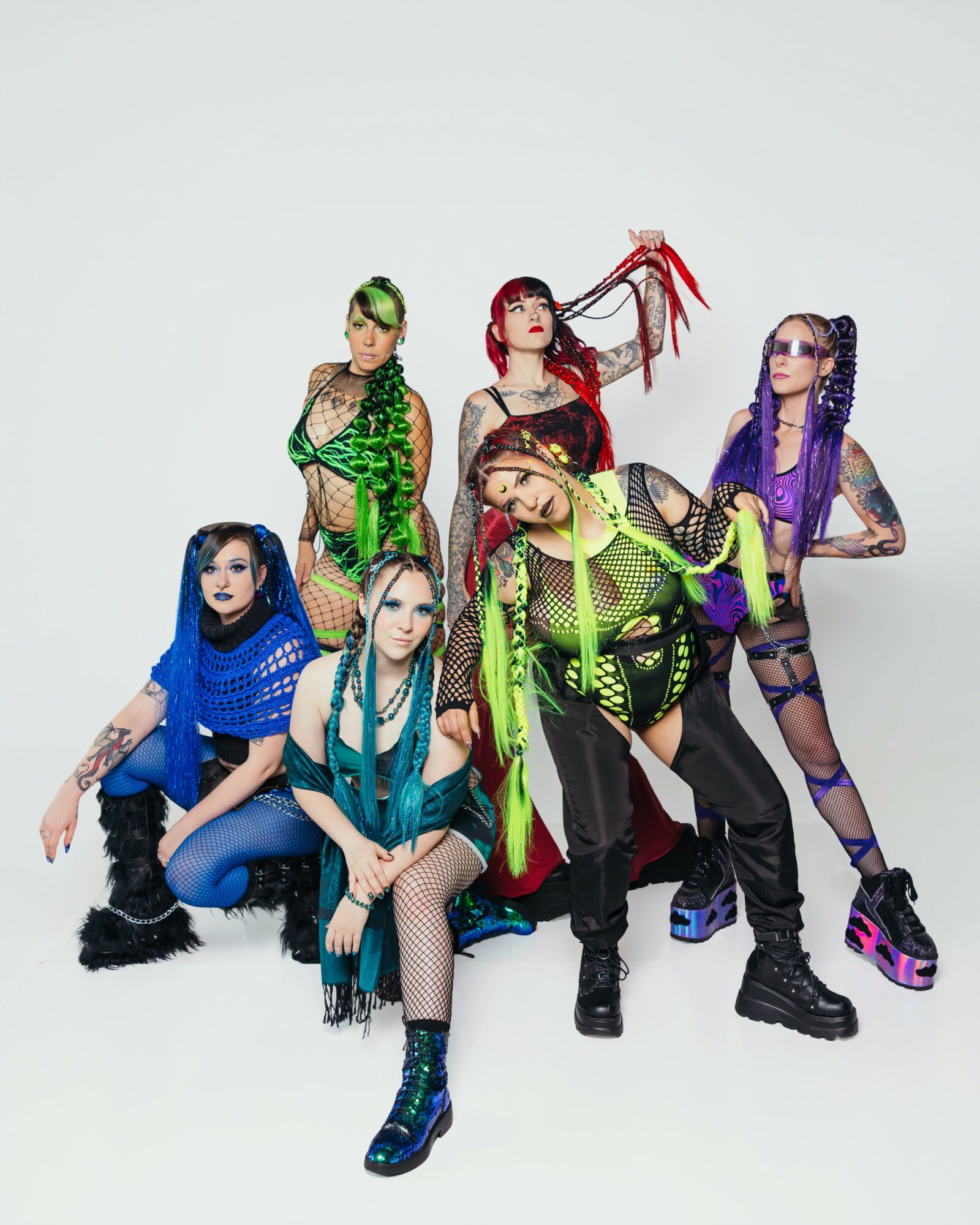 Six people in colorful, edgy outfits pose against a plain background, with varied hairstyles and accessories.