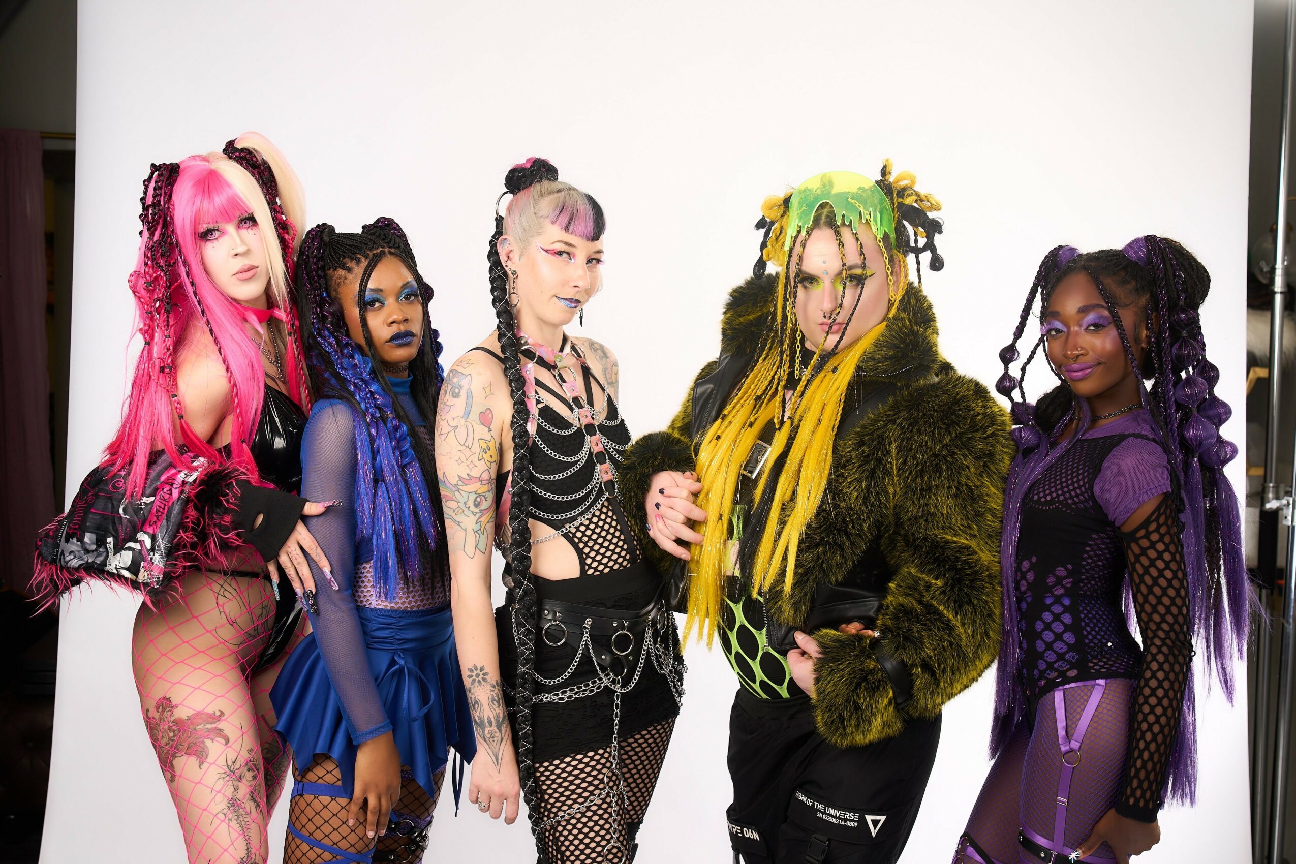 Five people with colorful hairstyles and fashion poses stand against a white background.