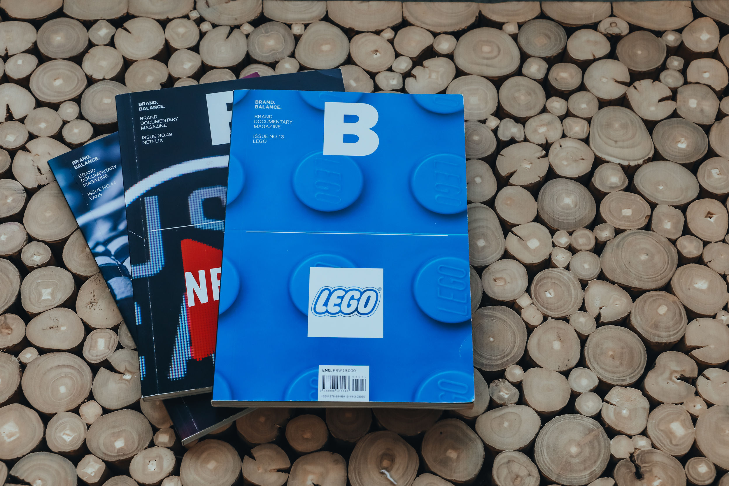 Three LEGO magazines on a bed of round white stones, with the top magazine showing a blue cover and LEGO logo.