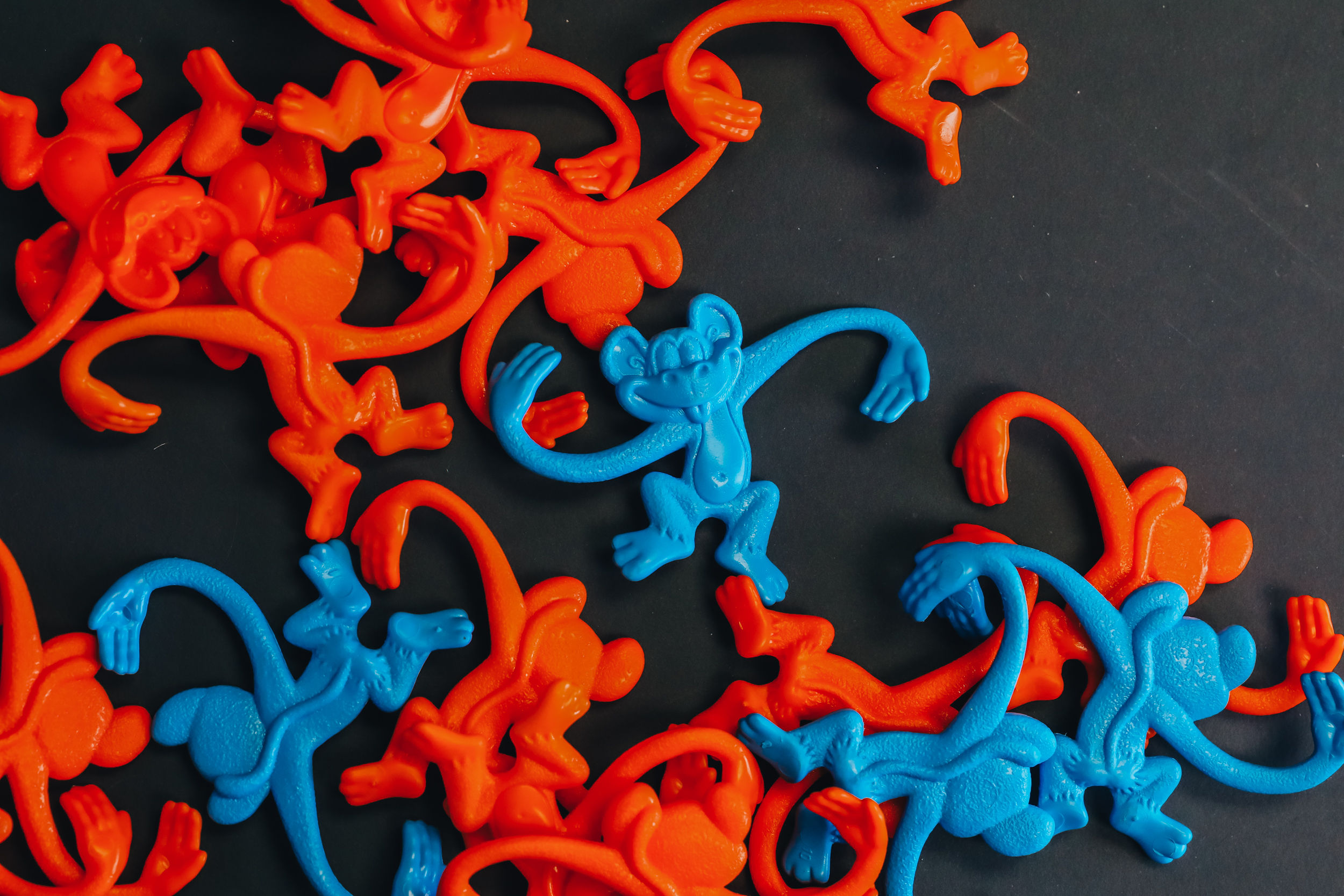 Colorful plastic monkey-shaped clips scattered on a dark surface, with some orange and blue clips intertwined.