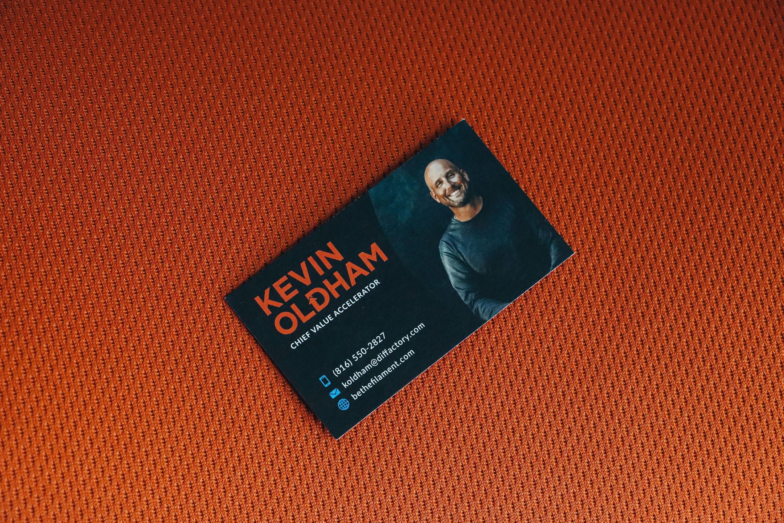 Business card with a photo of a smiling man, name Kevin Oldham, on a textured orange background.