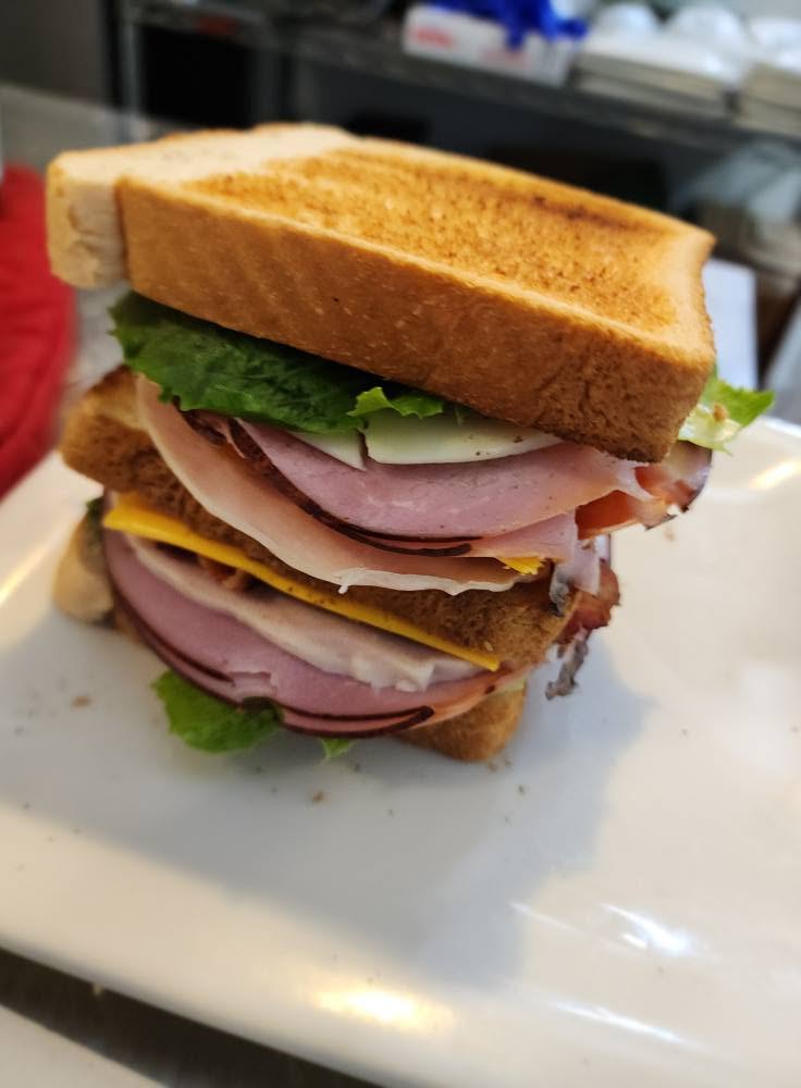 Sandwich with bread, lettuce, turkey, ham, and cheese on a white plate.