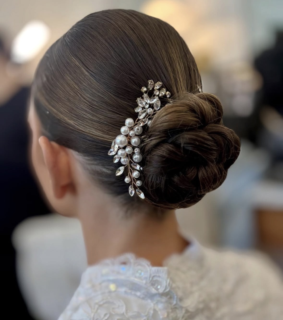 Elegant updo hairstyle with a decorative hairpiece, viewed from the back, on a woman with smooth, dark hair.