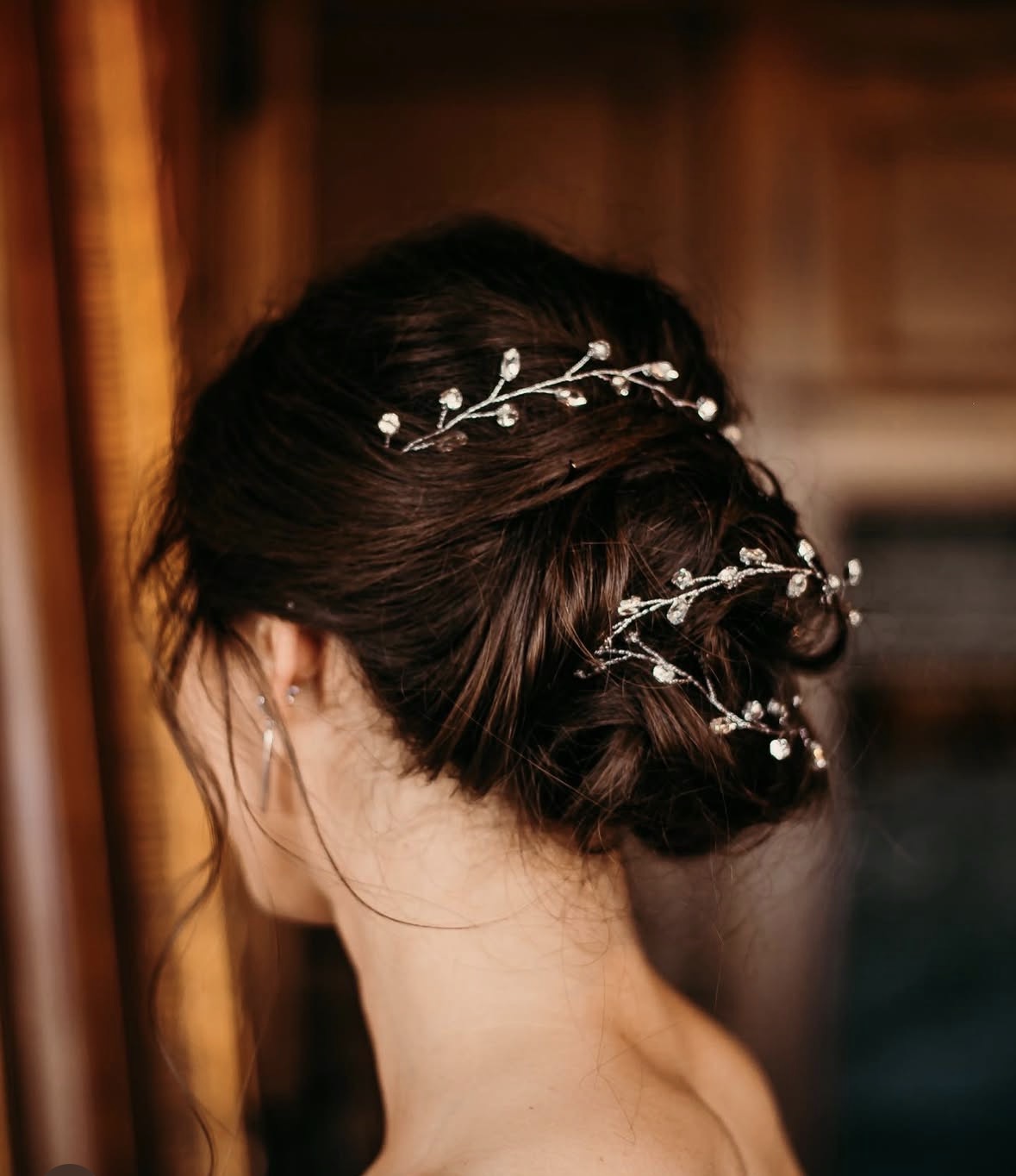 Updo hairstyle with decorative hair accessories featuring small white flowers and silver branches, viewed from the back.
