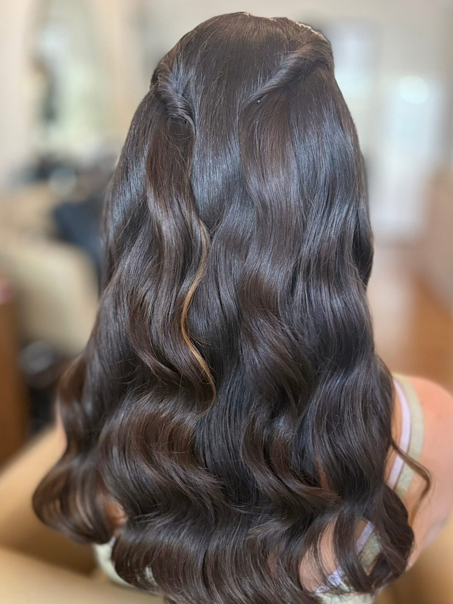 Back of a person with long, wavy, dark brown hair, styled in loose waves.