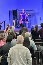 Performer on stage with a cage, audience watching, blue background, person wearing colorful clothing, stage setup visible.