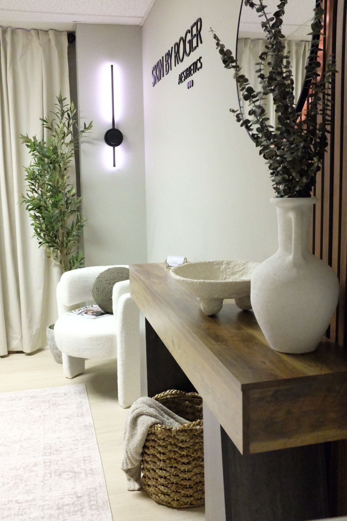 Interior view of a room with a wooden table, white chairs, a potted plant, and wall decor, seen from the side.