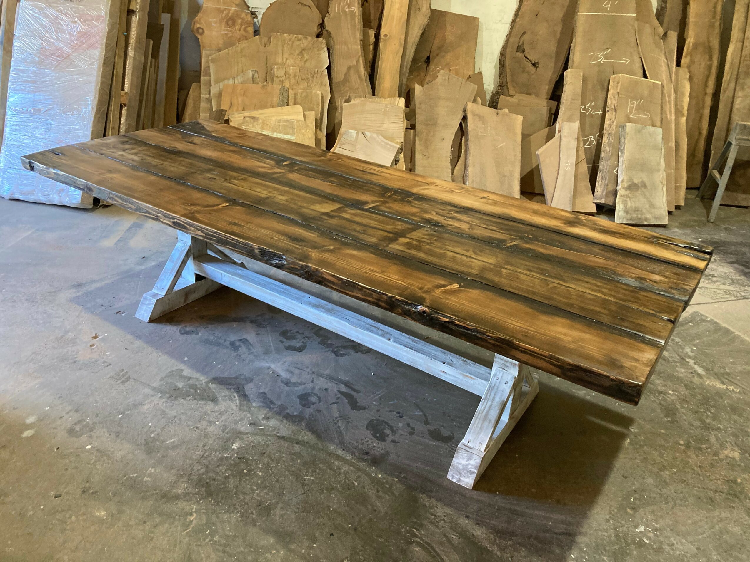 Wooden table with a dark, polished surface and metal legs in a workshop with wood pieces in the background.