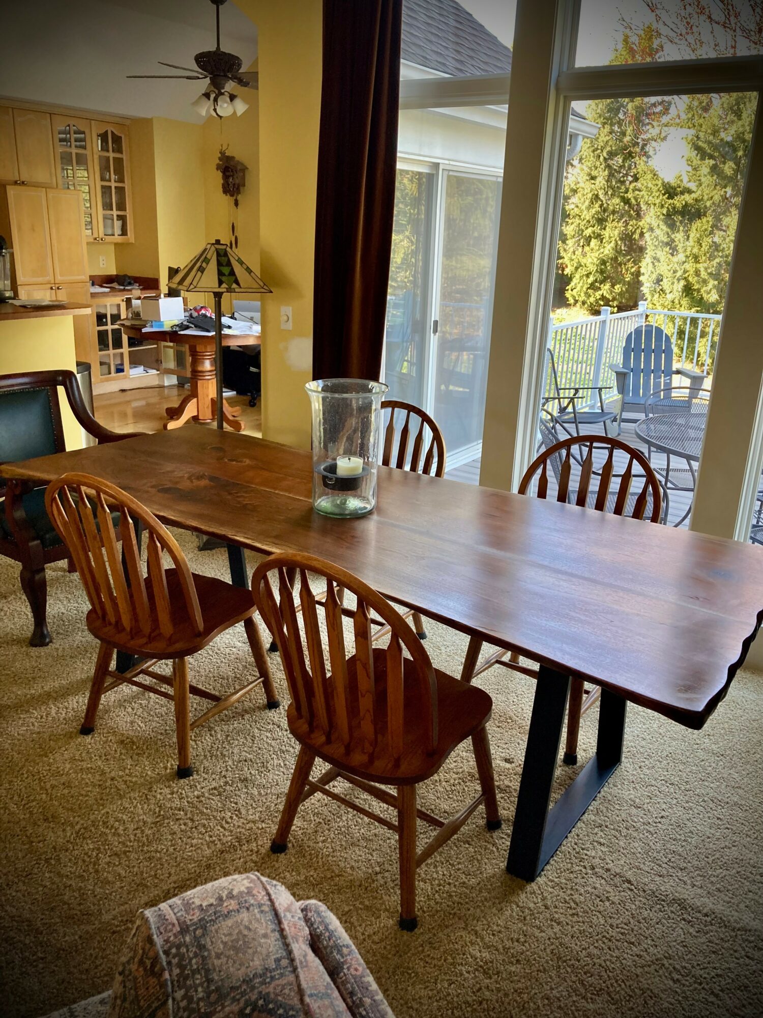 Dining room with wooden table and six chairs, large sliding glass door leading outside, sunlight, and a view of trees.