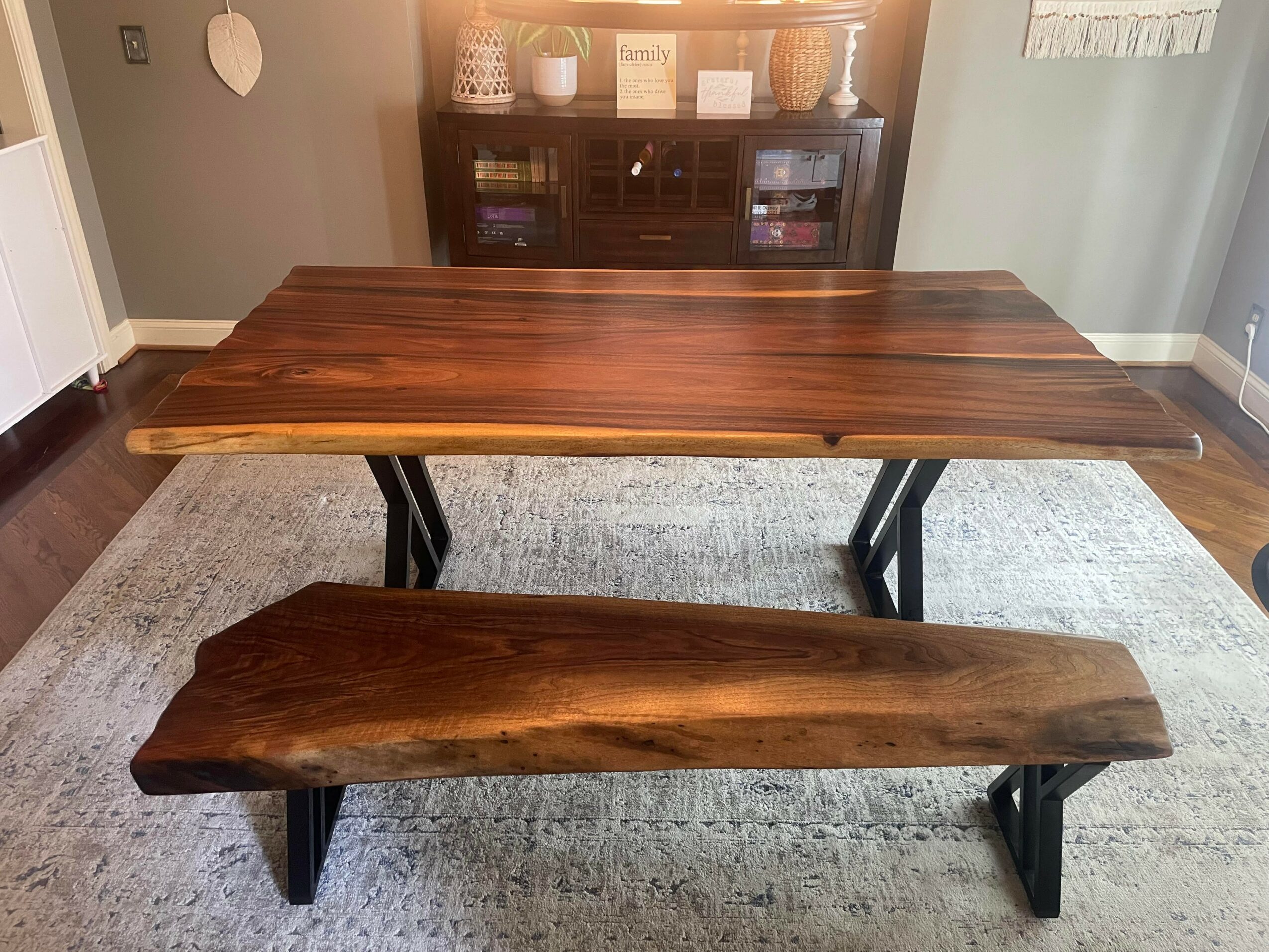 Wooden table with a matching bench on a light-colored rug in a room with a cabinet in the background.