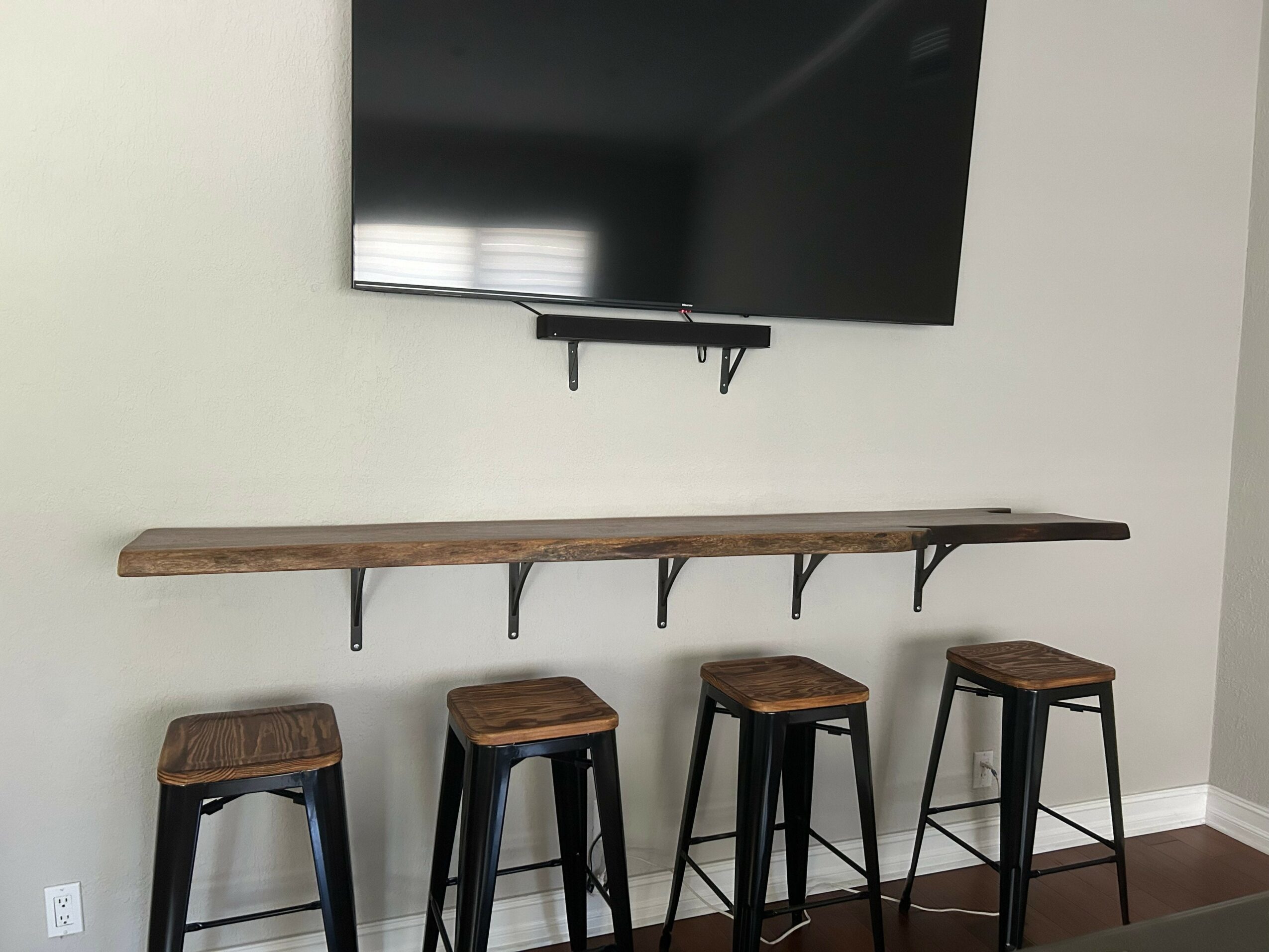 Flat-screen TV mounted on wall above a wooden shelf with four stools underneath.