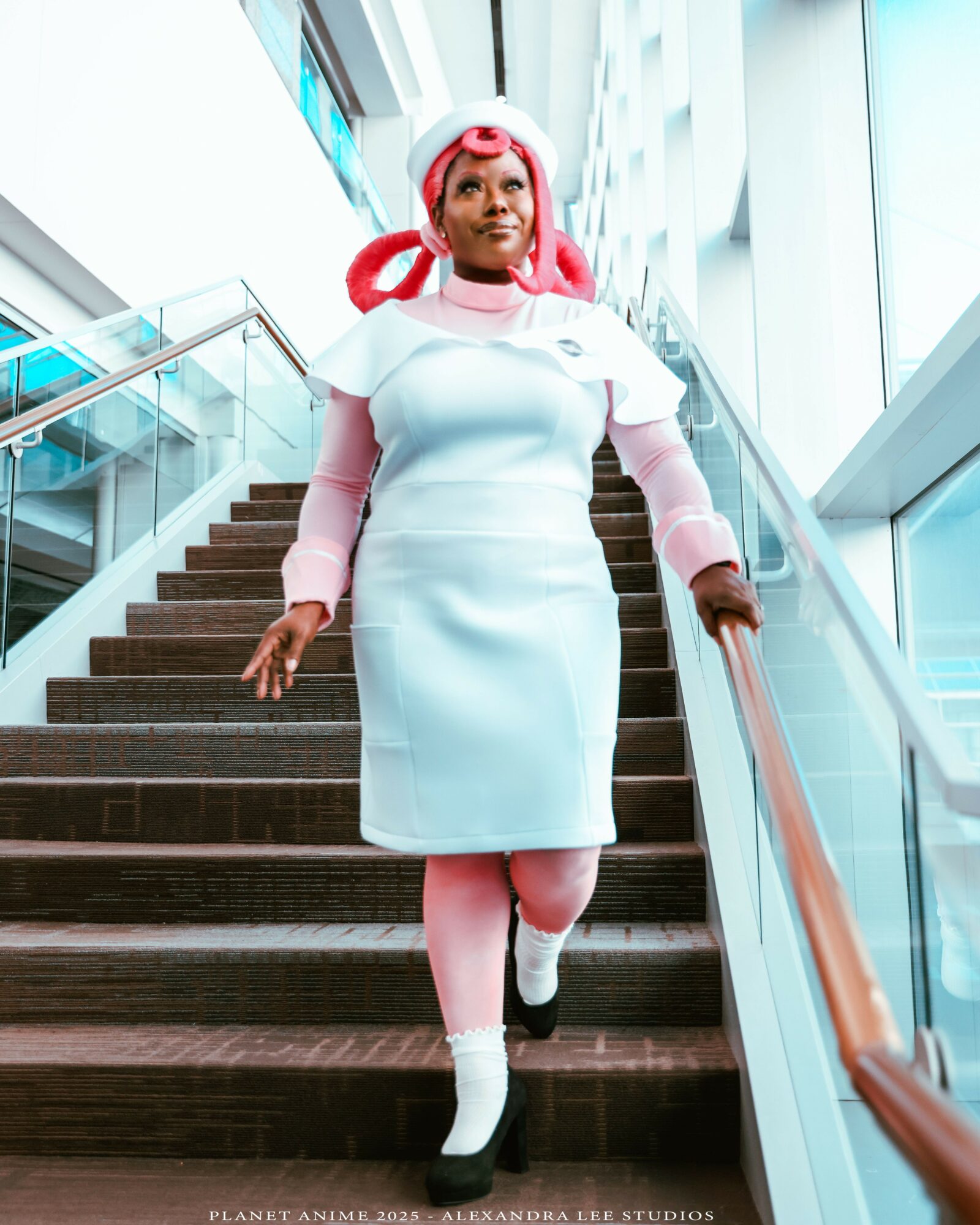Woman with pink hair and futuristic outfit walking down stairs in a modern building, glass walls and stairs visible.