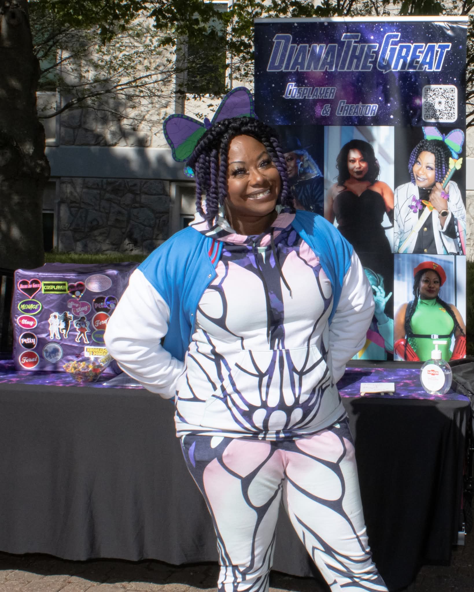 Woman in butterfly-themed outfit and hat standing outdoors with display and banner behind her.