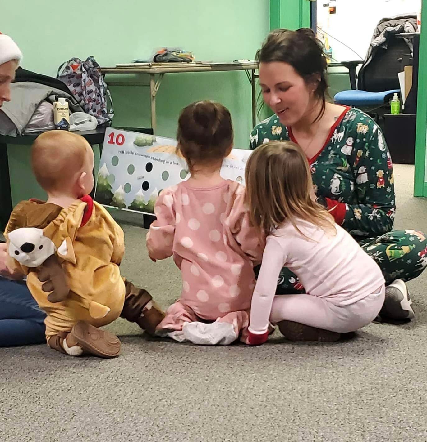 Woman with three children sitting on the floor indoors, one child in a lion costume, others facing her, engaging in activity.