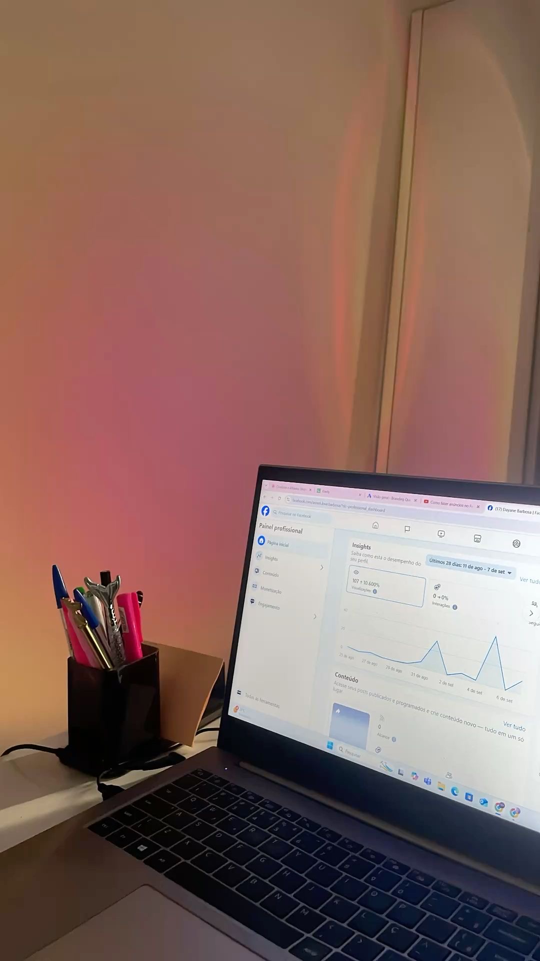 Laptop on desk displaying graphs and data, with a container of pens nearby, against a plain wall background.