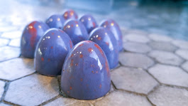 Group of shiny blue eggs with red speckles on a hexagonal tiled surface.